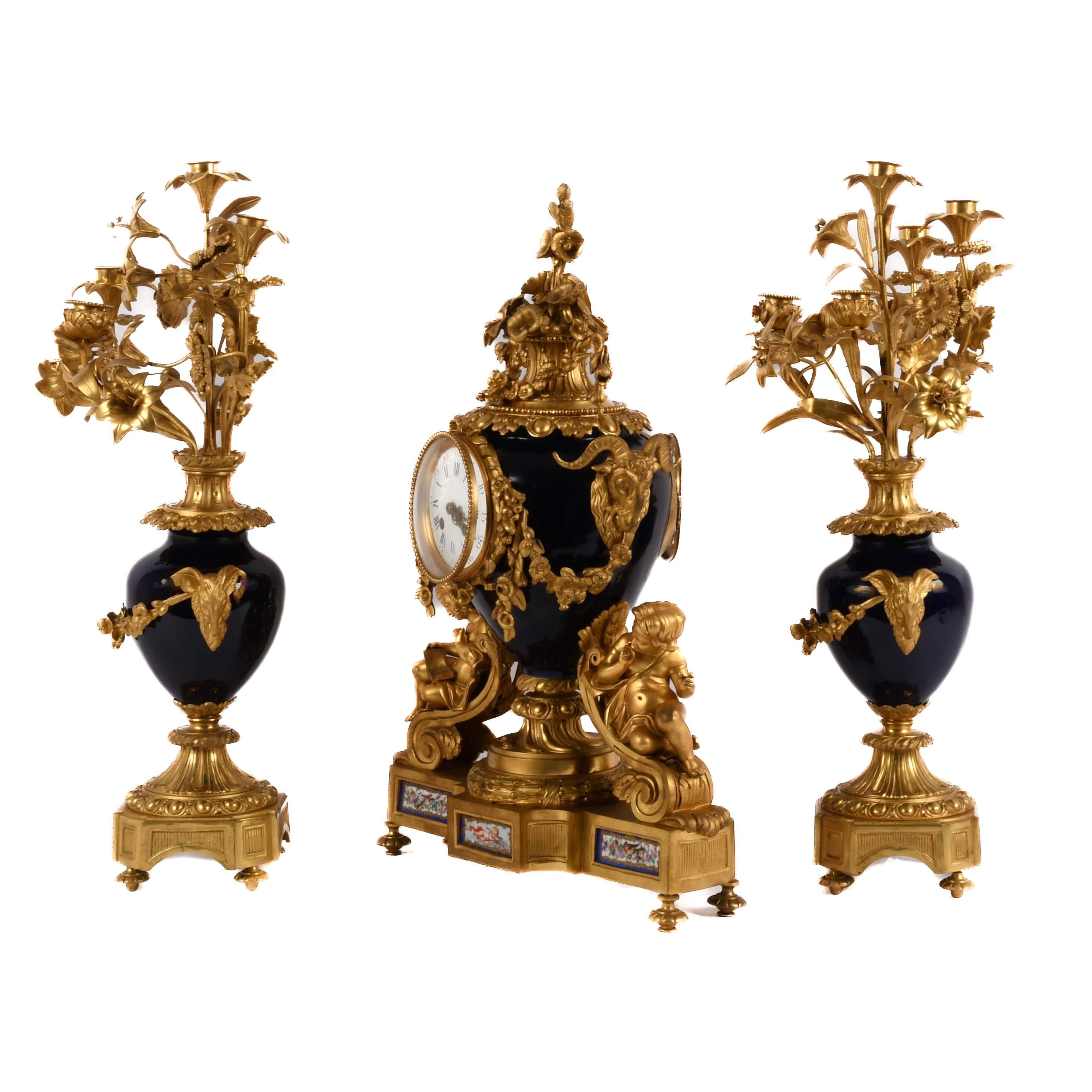 This antique French clock set by Japy Frères is a stunning example of Belle Époque craftsmanship, blending deep cobalt porcelain with finely gilded bronze. The central clock, adorned with cherubs and floral garlands, is flanked by matching