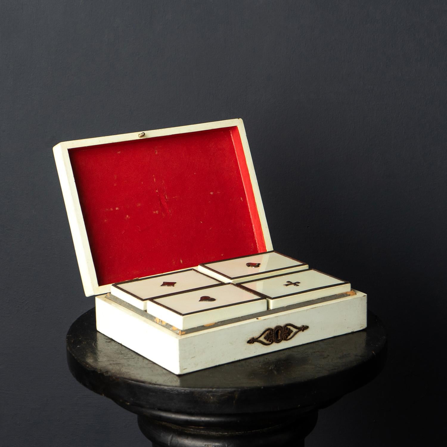 Antique gaming casket with gaming tokens
An unusually white lacquered wooden box with decorative metal mounts which opens up to reveal a red-fitted interior with four removable internal compartments each representing the four different suits,