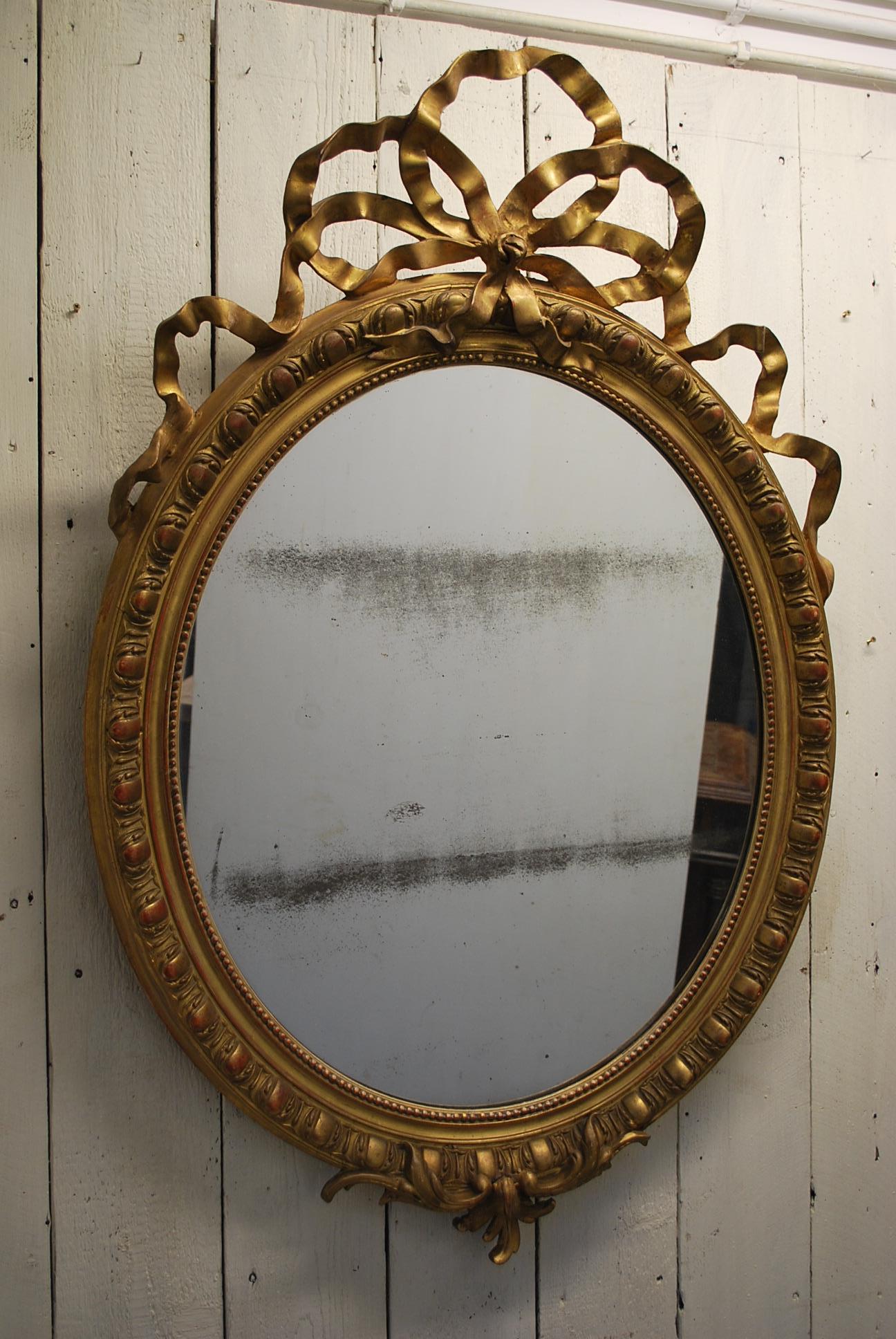 This is a large 19th century, French antique overmantle mirror with a ribbon crown and an egg and dart border. Original foxed looking glass and lovely old pine back.