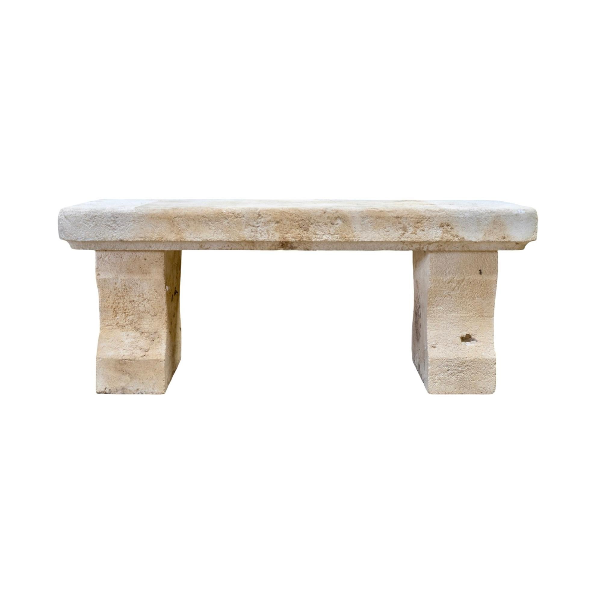 A timeless 18th-century French limestone bench, hand-carved from solid stone with a beautifully aged surface and naturally weathered patina. Its simple, monolithic silhouette features a thick rectangular seat supported by two sturdy, block-style