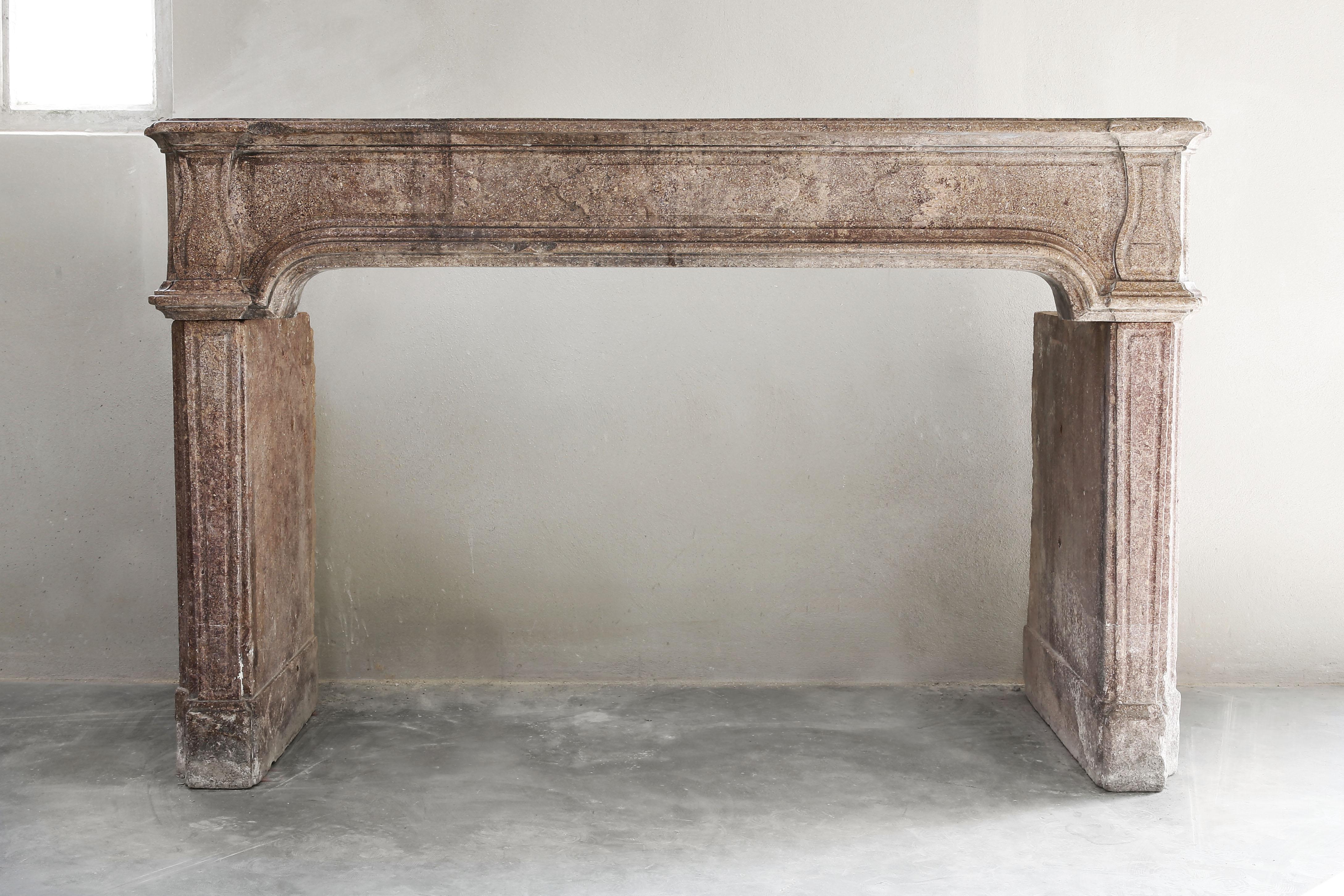 Beautiful French antique marble stone fireplace from the 19th century, time of Louis XIV. This fireplace has beautiful curves and lines and a warm color scheme. The color is a melange of brown/beige. The legs are straight and in the middle of the
