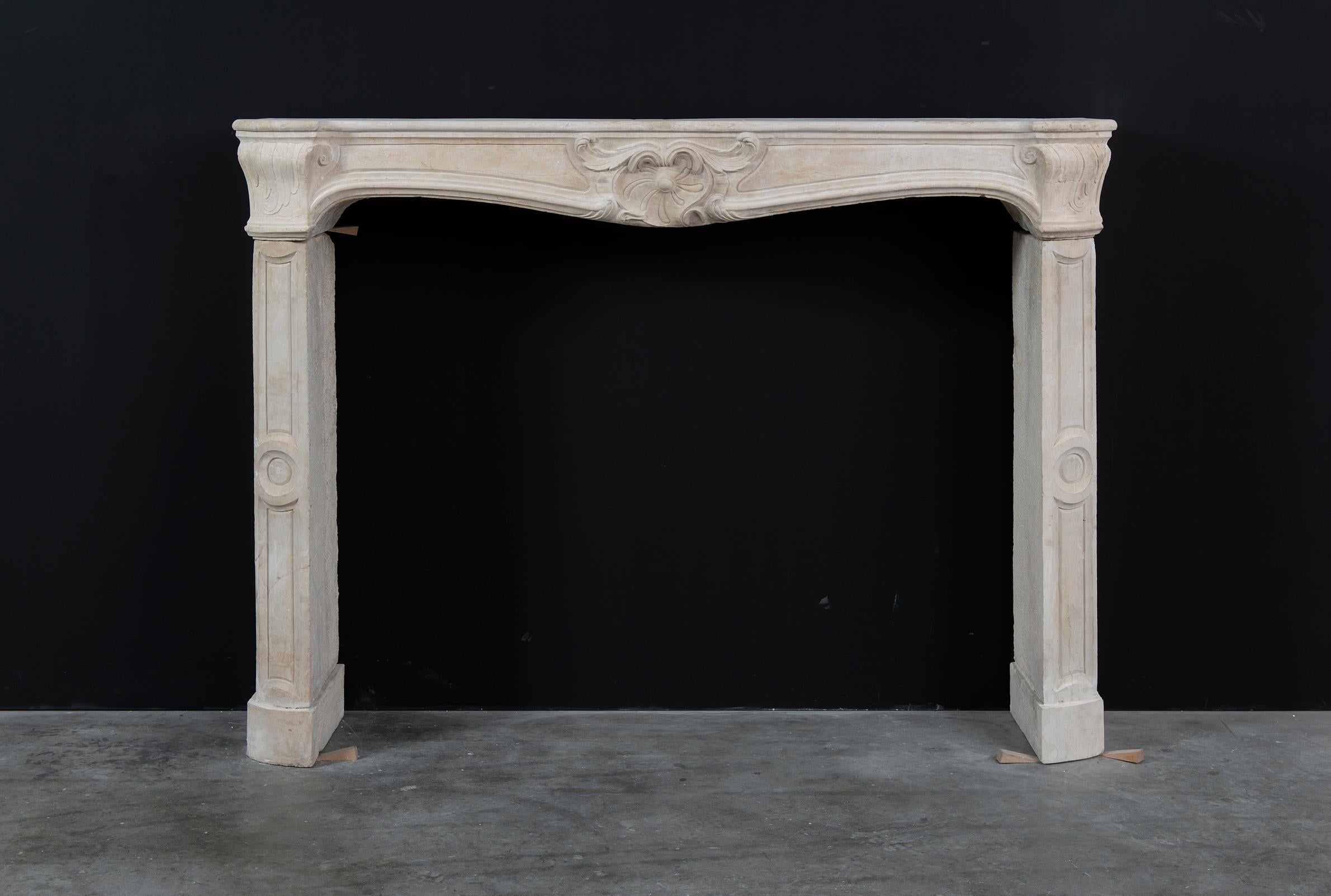 An early 19th century French Louis xv limestone fireplace mantel. 

The moulded and profiled shelf is integral to the frieze which is centred by a beautiful acymetrical shell and is carved from the solid. 
The curled leaf endblocks are supported by