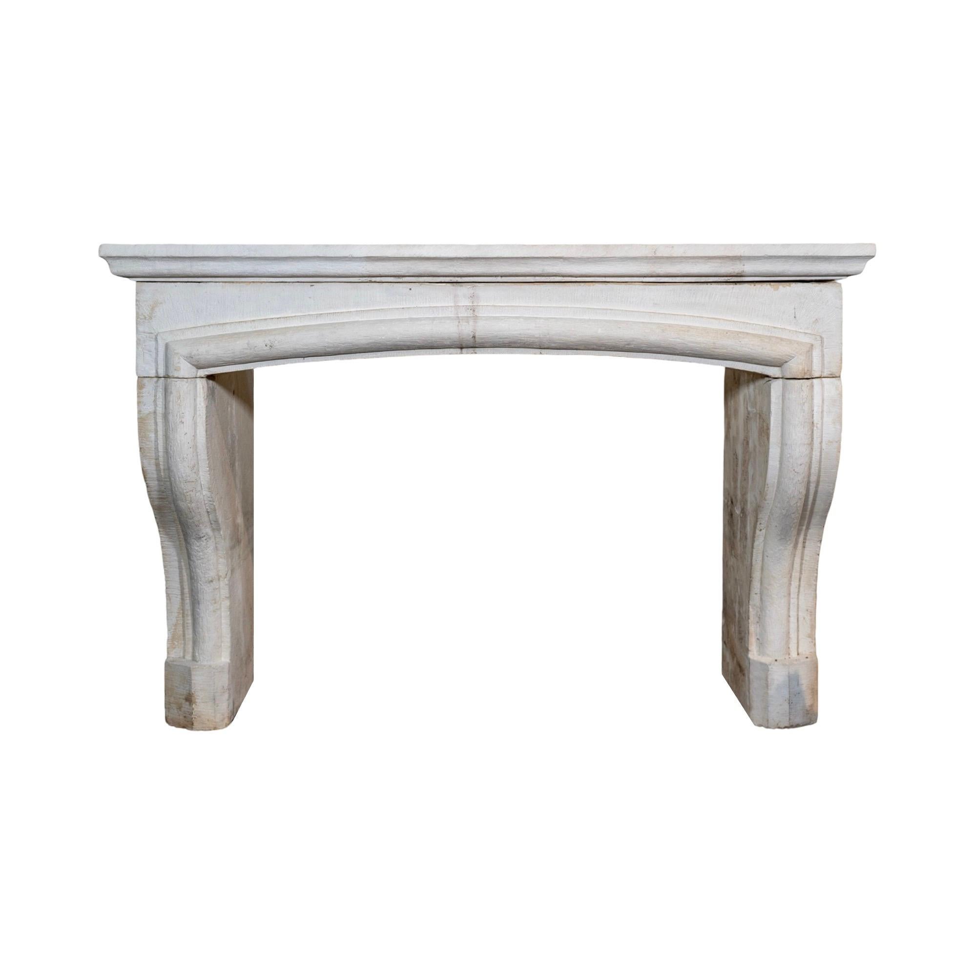 An 18th-century French limestone mantel featuring a gracefully carved bolection arch design that extends across the center and down both legs. Aged patina and timeworn character add to its historic charm, showcasing centuries of authenticity. 