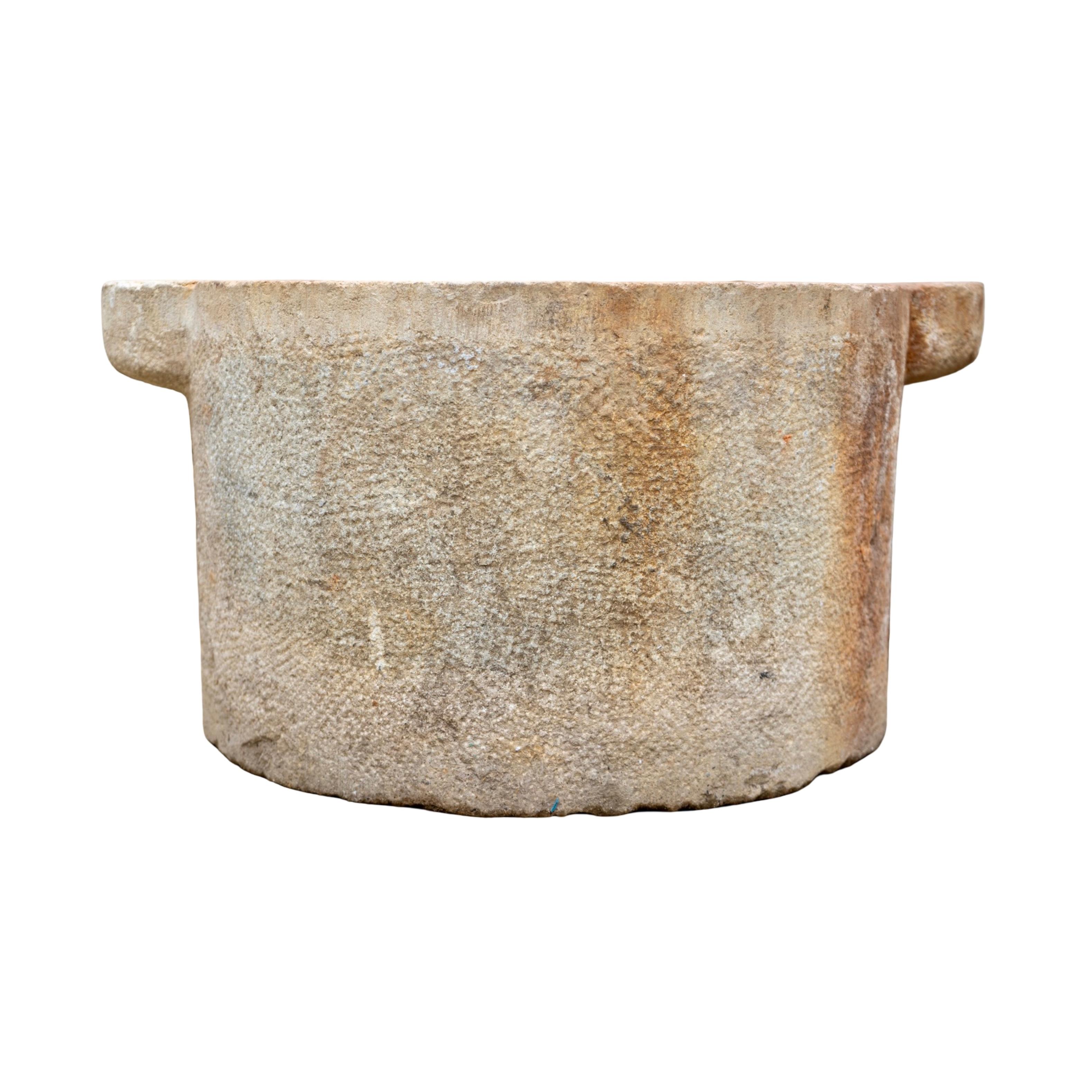 Sculptée à la main en France au cours du XIXe siècle, cette auge ancienne en pierre calcaire recyclée présente une forme circulaire classique avec de solides pattes latérales. La pierre a développé une patine chaude et usée par le temps avec une
