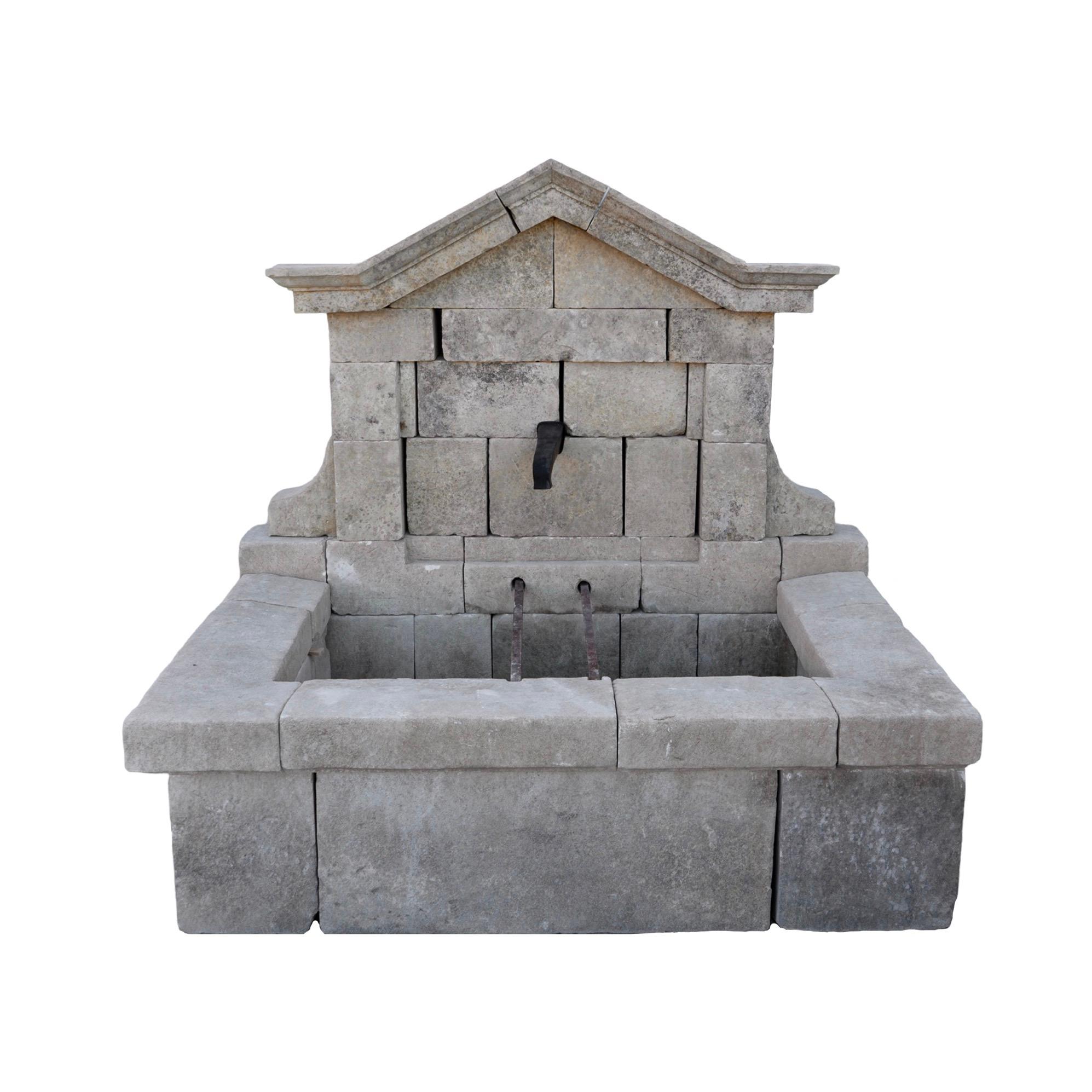 Antigua fuente de pared de piedra caliza de la Francia de principios del siglo XX, con una pila rectangular de generosas dimensiones diseñada para el desbordamiento del agua. El panel de pared presenta un elegante diseño arqueado e incluye un