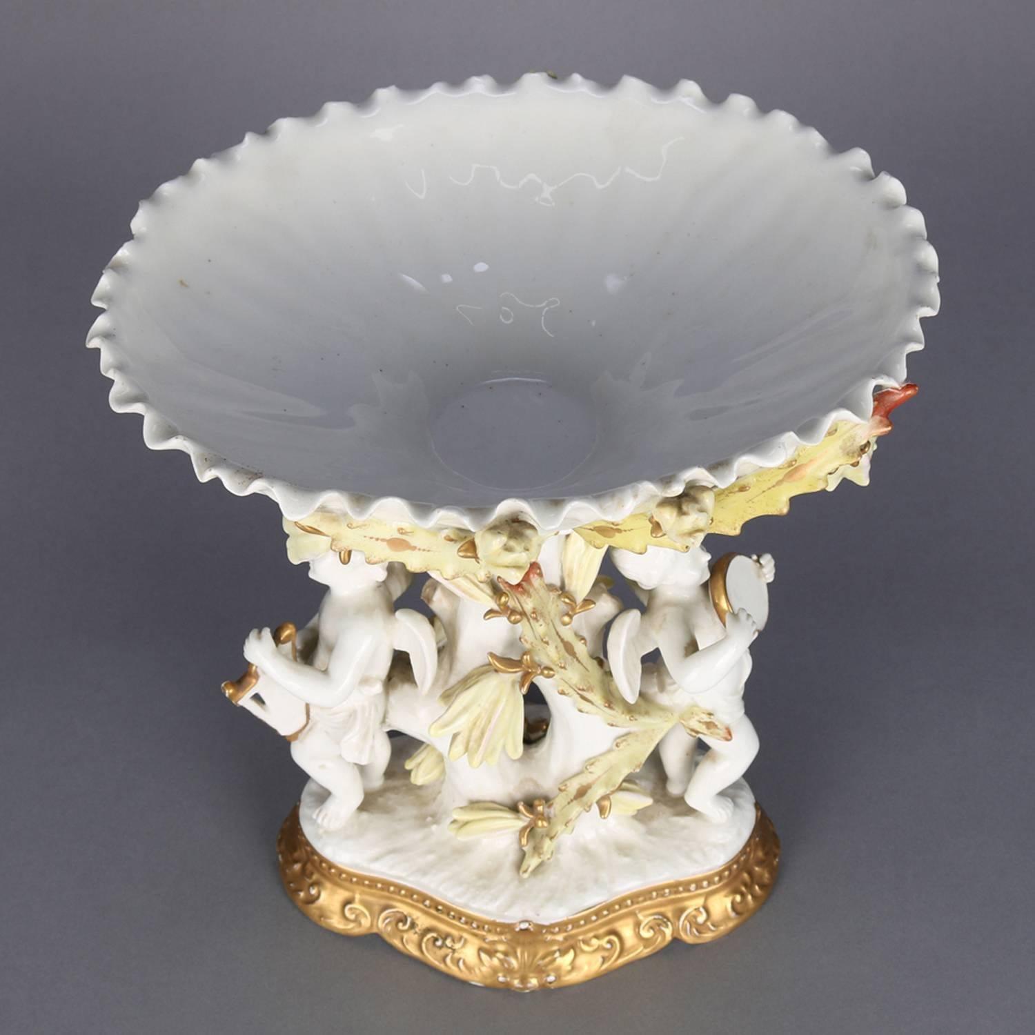 Antique Classical French Limoges school porcelain figural compote features ruffled bowl decorated with floral and foliate swags and supported by woodland branch form pedestal with winged cherubs playing musical instruments and seated on scroll and