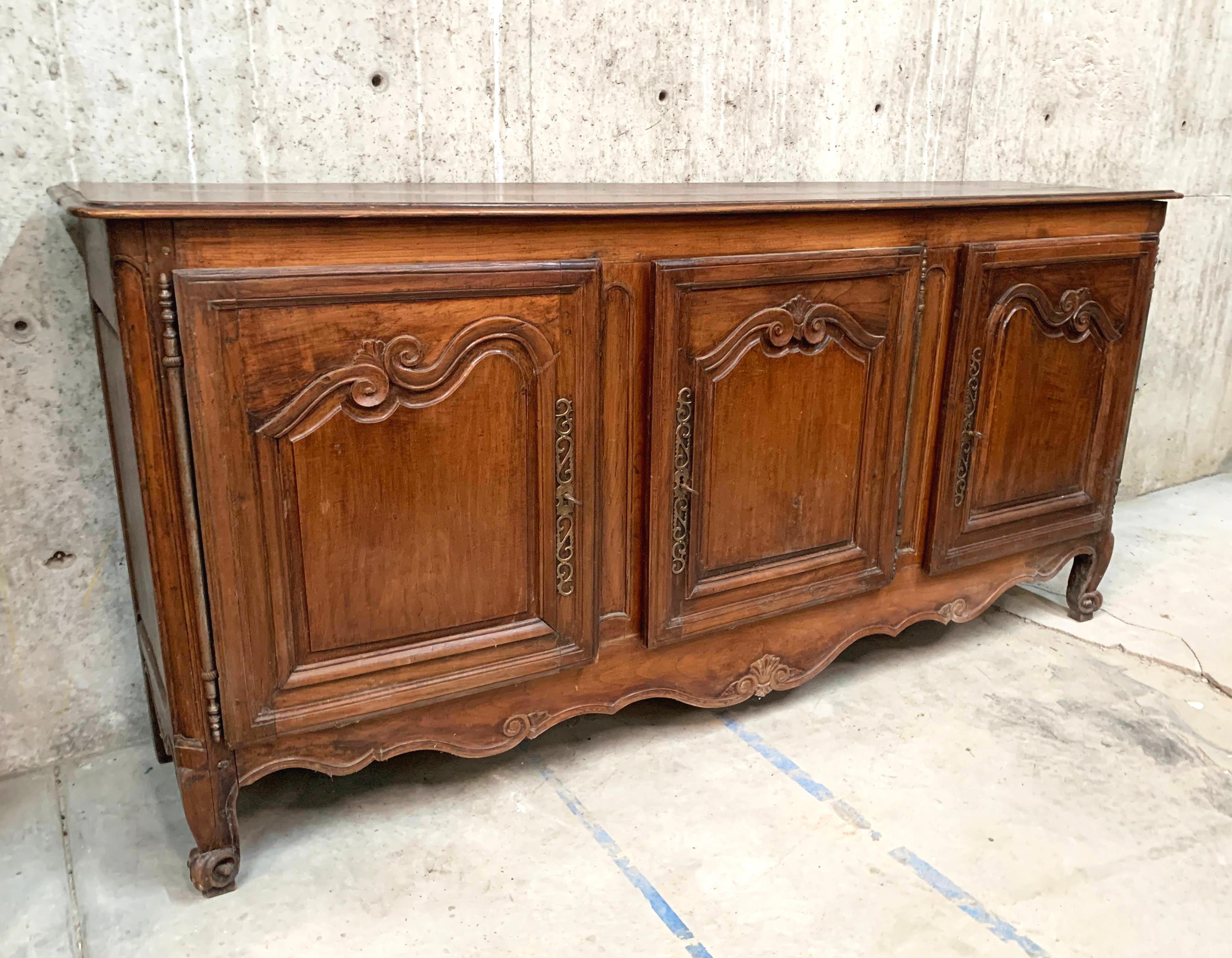 French Provincial fruitwood sideboard, early 19th c., long rectangular case fitted with three cabinet doors, carved scroll motif on buffet doors, scalloped apron, rising on cabriole legs, ending in whorl feet. The fruitwood has a lovely patina, as