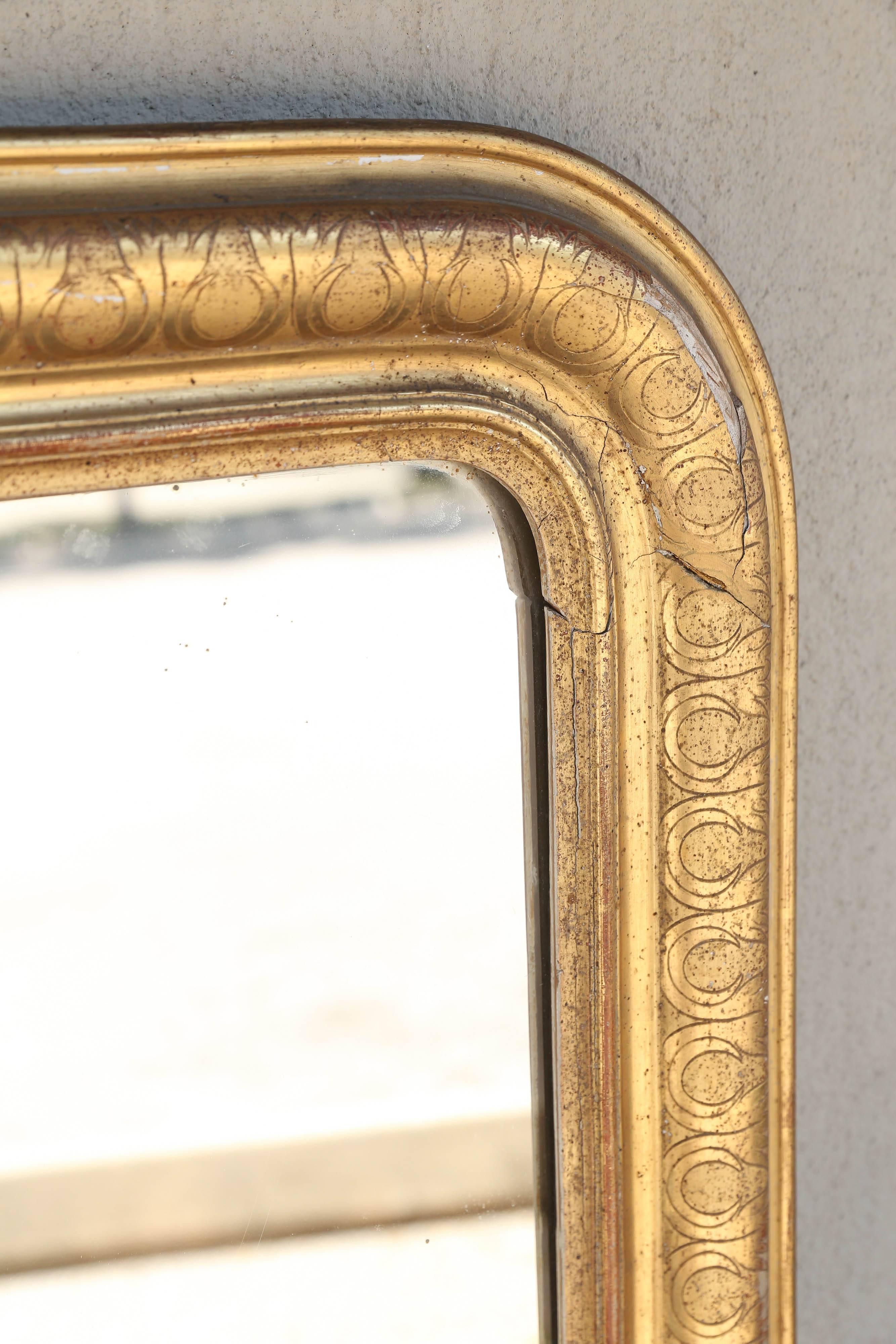 This antique French mirror features a wonderful carved, gilt frame with a gorgeous nouveau pattern. The inter-locked pattern looks both geometric and organic. Touches of reds and greens also show through the gilt. Entire back is enclosed (shown).