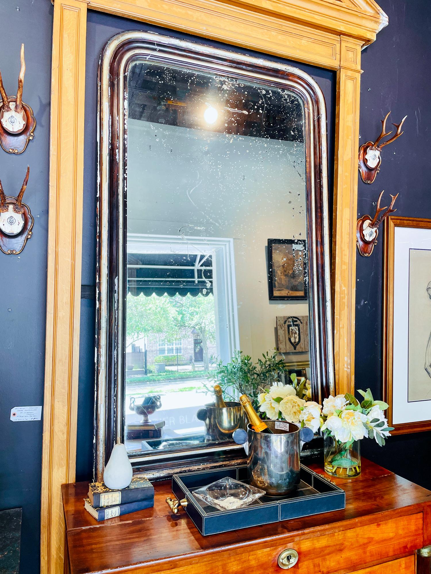 This is an antique Louis Philippe mirror from France. The frame of the mirror has a black lacquered finish with champagne colored gilt and a marbled brown and black pattern that mimics a woodgrain look. The glass is original and has several areas of