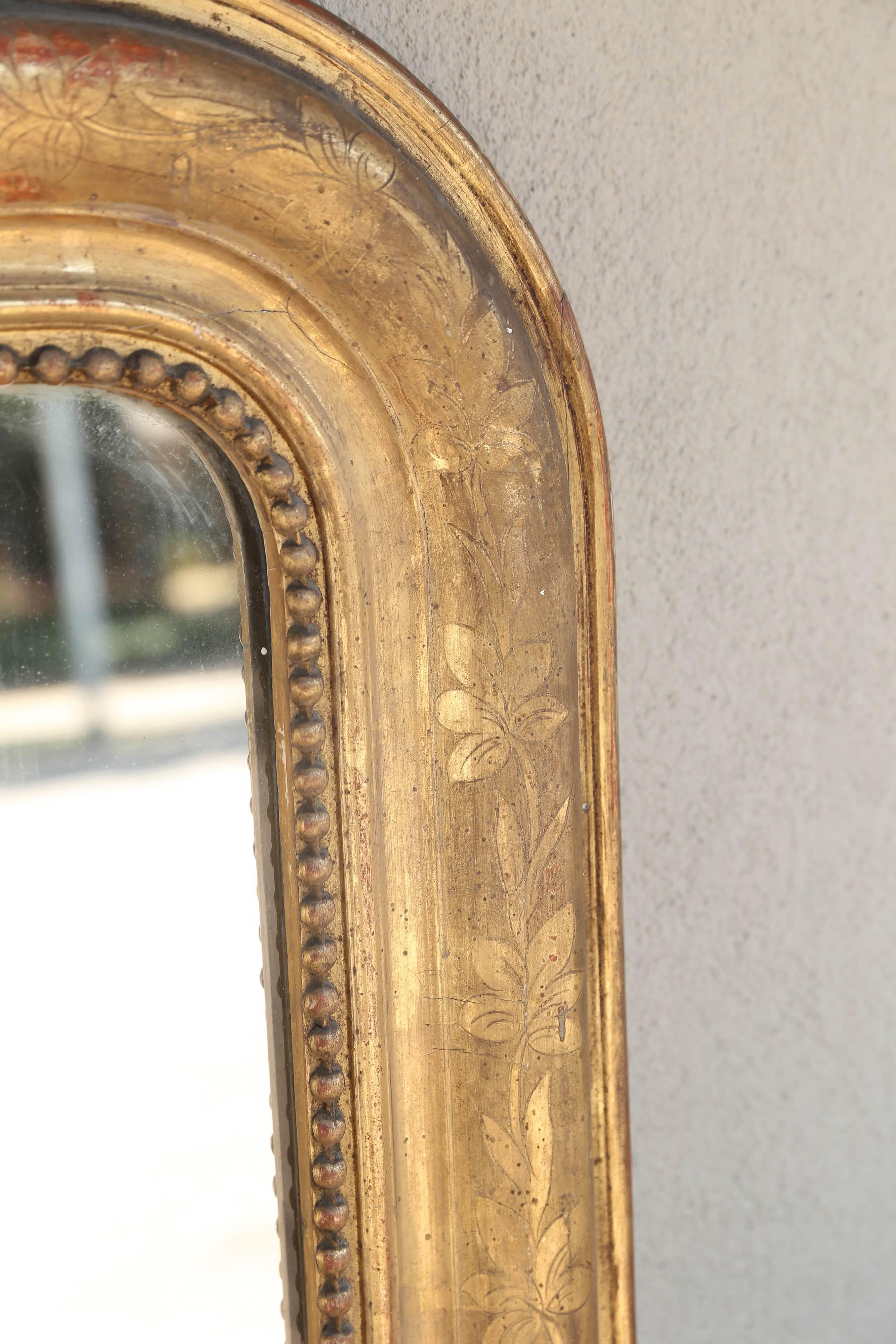 This is an antique Louis Philippe Mirror, discovered in France. The design on the giltwood frame is a floral pattern with decorative beaded accents. The tones are in the range of soft reds that have likely faded over time, leaving a beautiful