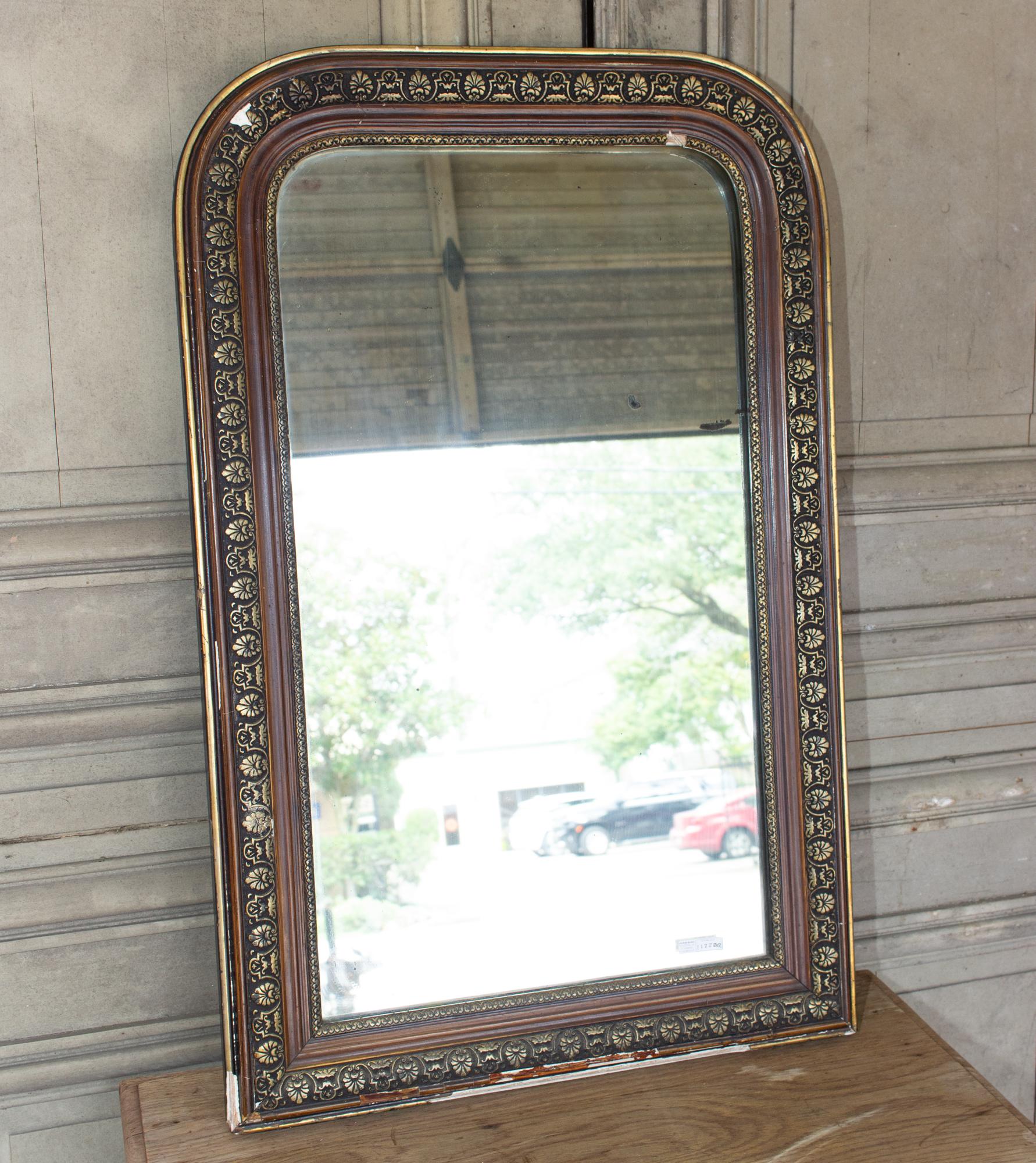 This is an antique Louis Philippe mirror, discovered in France. The design on the giltwood frame is a floral decorative pattern with repeating shell-shaped accents and a textured gilt edge surrounding the mirror. The frame has been painted with deep