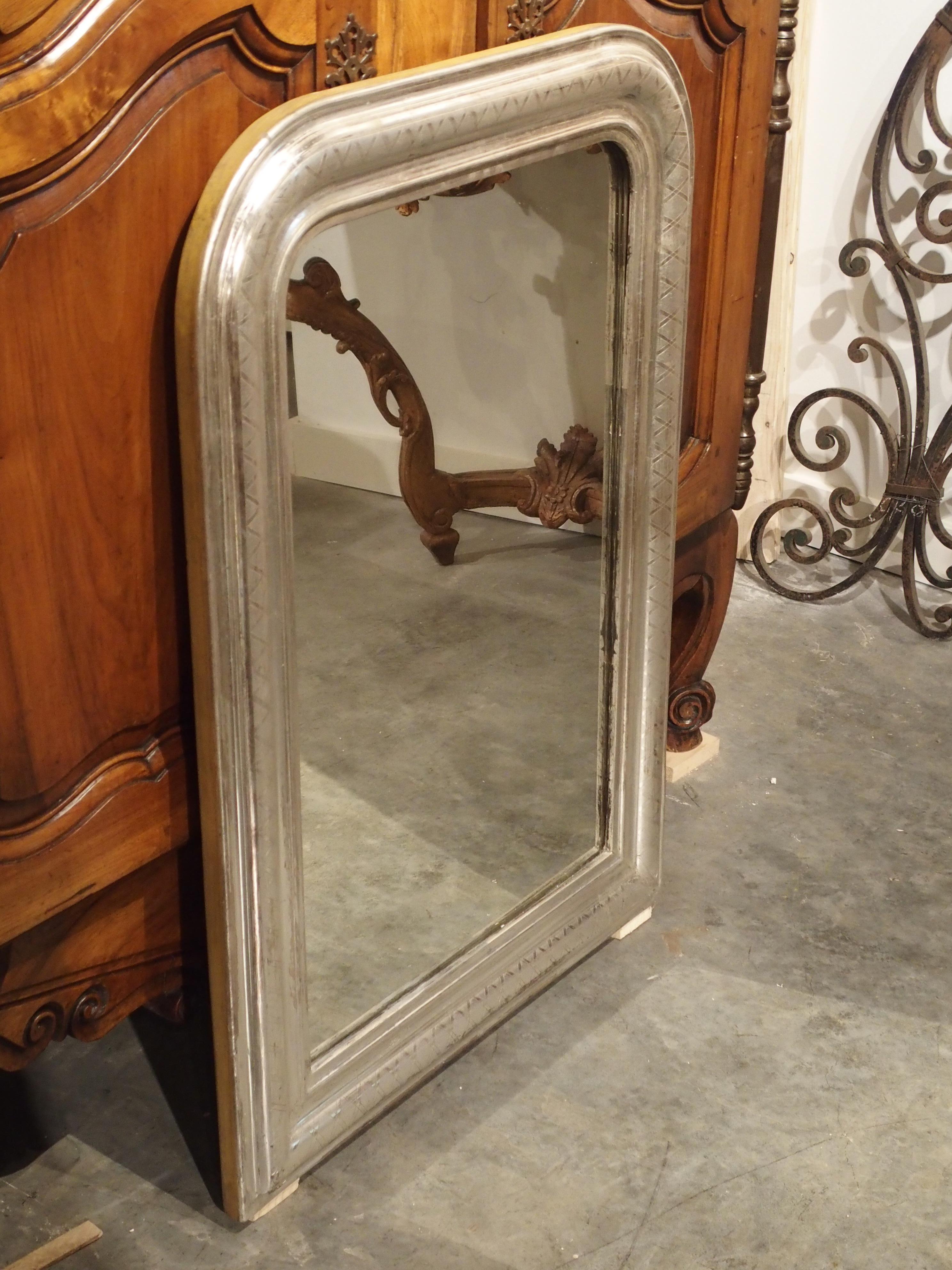 Versatile in its design and function, this silverleaf Louis Philippe mirror can be used in a modern or antique setting. The raised center section of this Louis Philippe has linear ornamentation of gadrooned X’s. The adjacent moldings are indented