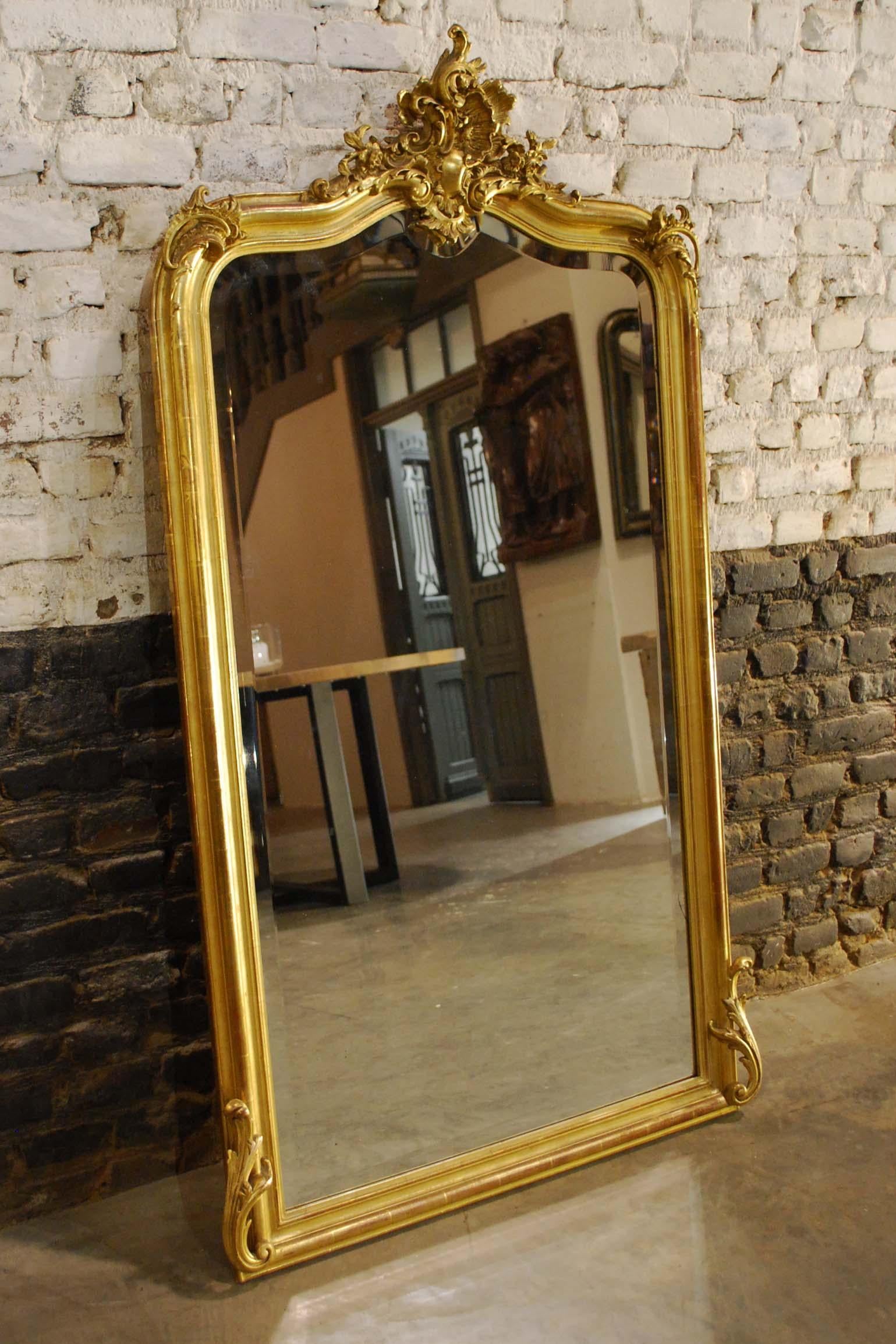 This beautiful antique French gold gilt mirror is a typical Louis Quinze or rococo mirror. 
It has the typical asymmetrical ornamentation and facetted mirror glass. The serpentine shaped top has rich ornamentation, depicting c-scrolls, accanthus,