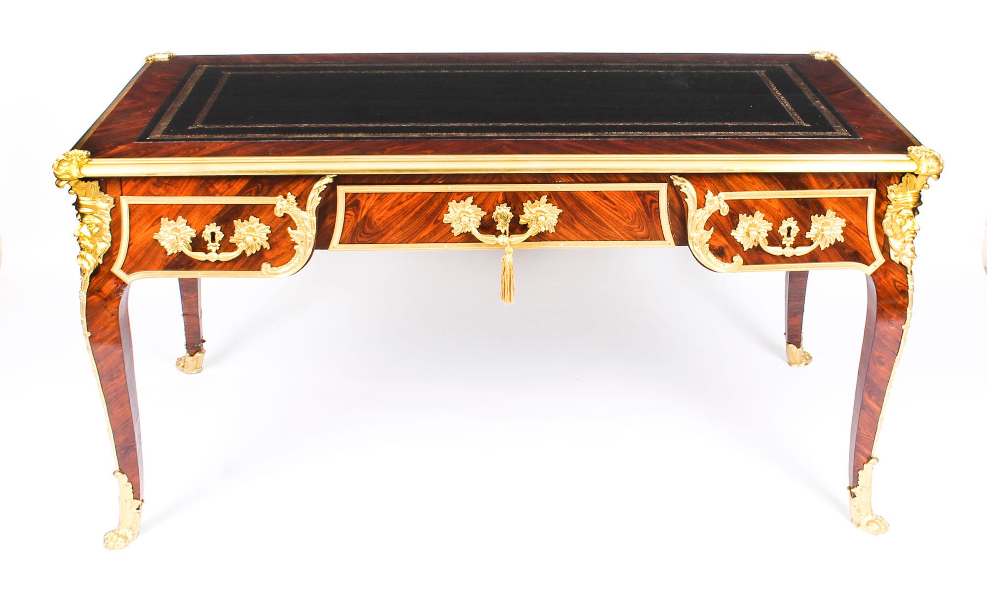 This is a gorgeous antique French Louis Revival gilt bronze mounted kingwood bureau plat, circa 1860 in date.

The shaped top has a decorative gilt bronze border, raised corner cartouches and an inset gold tooled black leather writing surface, above
