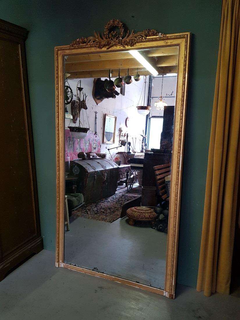 Large size antique French mercury mirror in Louis Seize style with gilded plaster frame with various ornaments on top including palm branches, flower buds etc., the original mercury mirror is still there. The frame has some damage all around and the