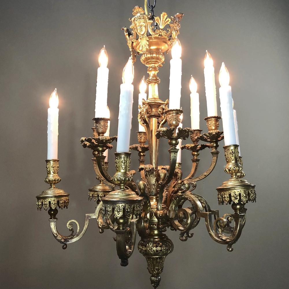 Antique French Louis XIV bronze chandelier is an exquisite example of the metalsmith's art, with intricate detailing from the angels' heads above to the tips of the gracefully scrolled arms with banner motif appearing to hang from the bobeches.