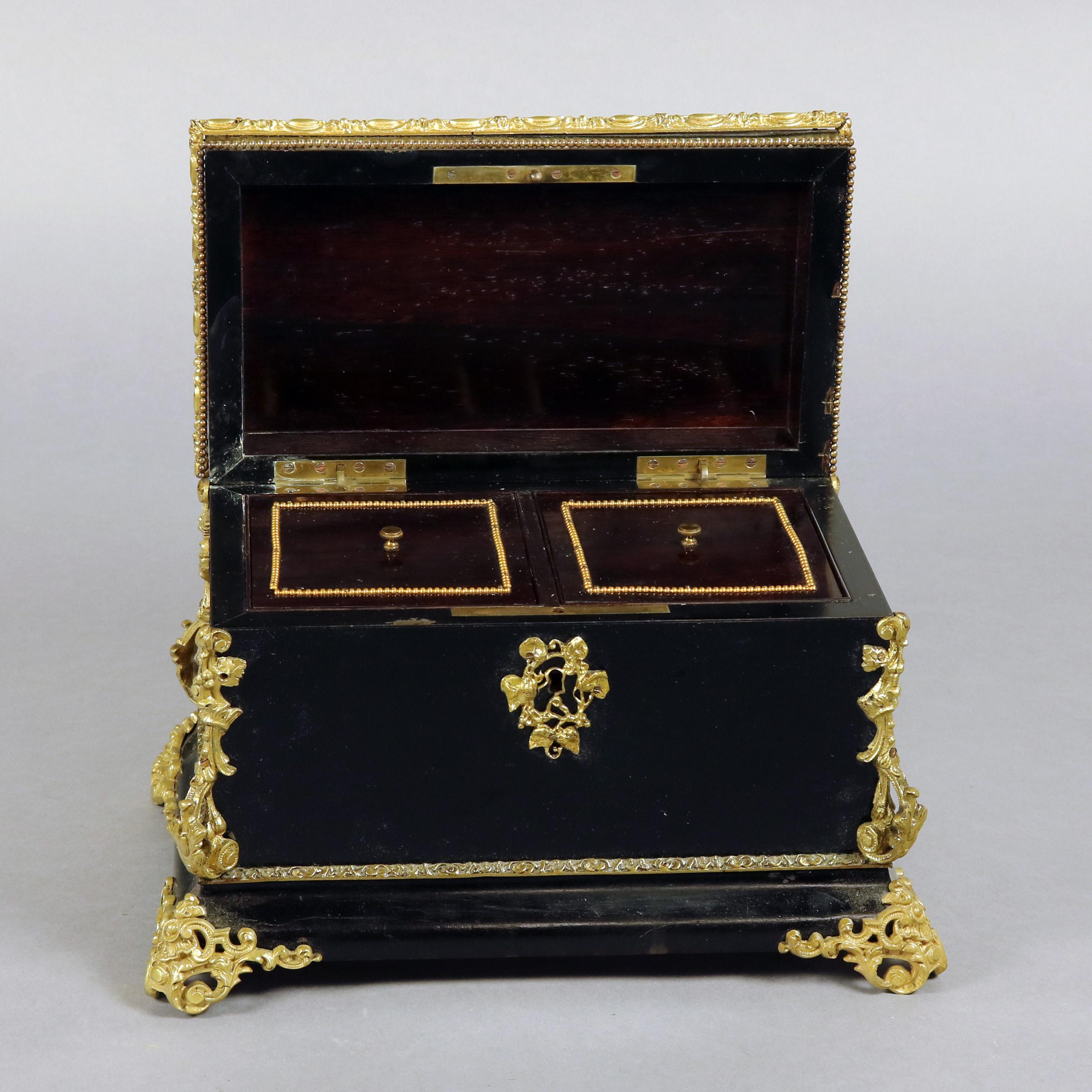 An antique French Louis XIV style tea caddy features ebonized cabinet having hinged and locking lid with central Sevres School hand painted floral porcelain reserved and foliate form cast ormolu mounts, escutcheon and feet, interior with two tin