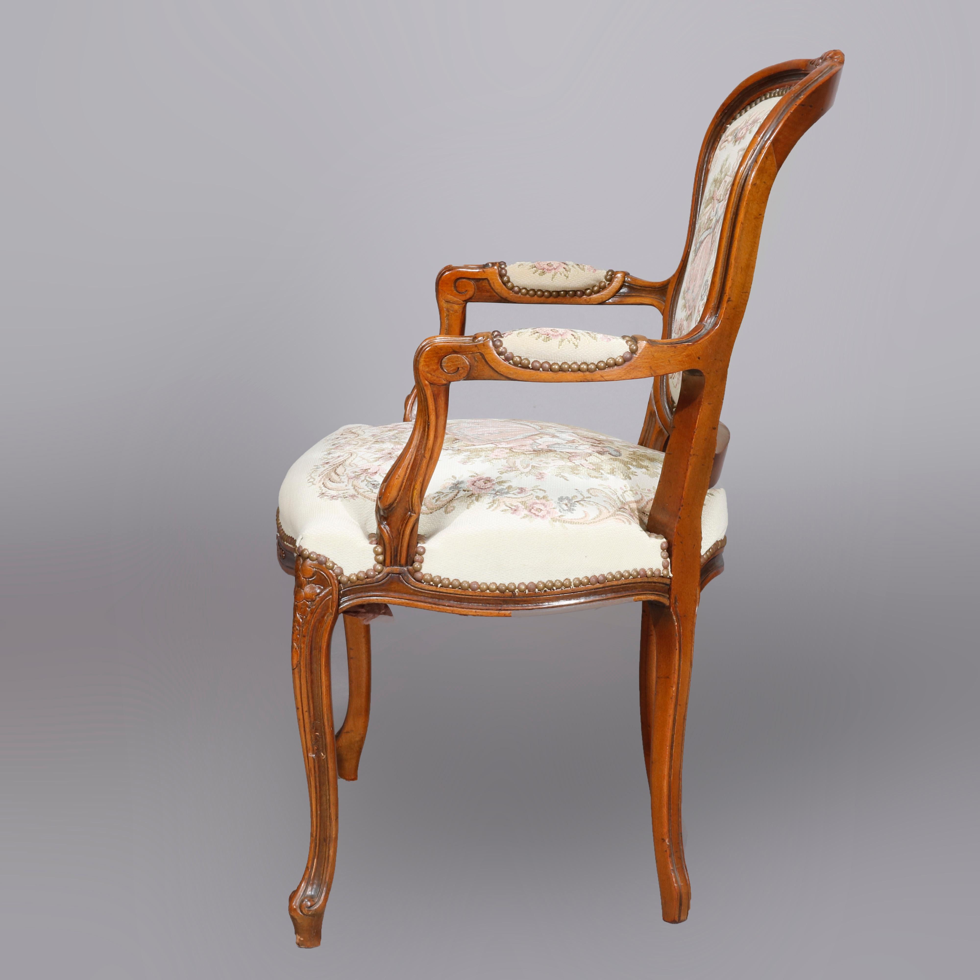 An antique French Louis XIV fauteuil armchair offers walnut construction with carved floral and scroll decoration with pictorial tapestry back and seat having courting scene in countryside setting, raised on cabriole legs terminating in scroll feet,