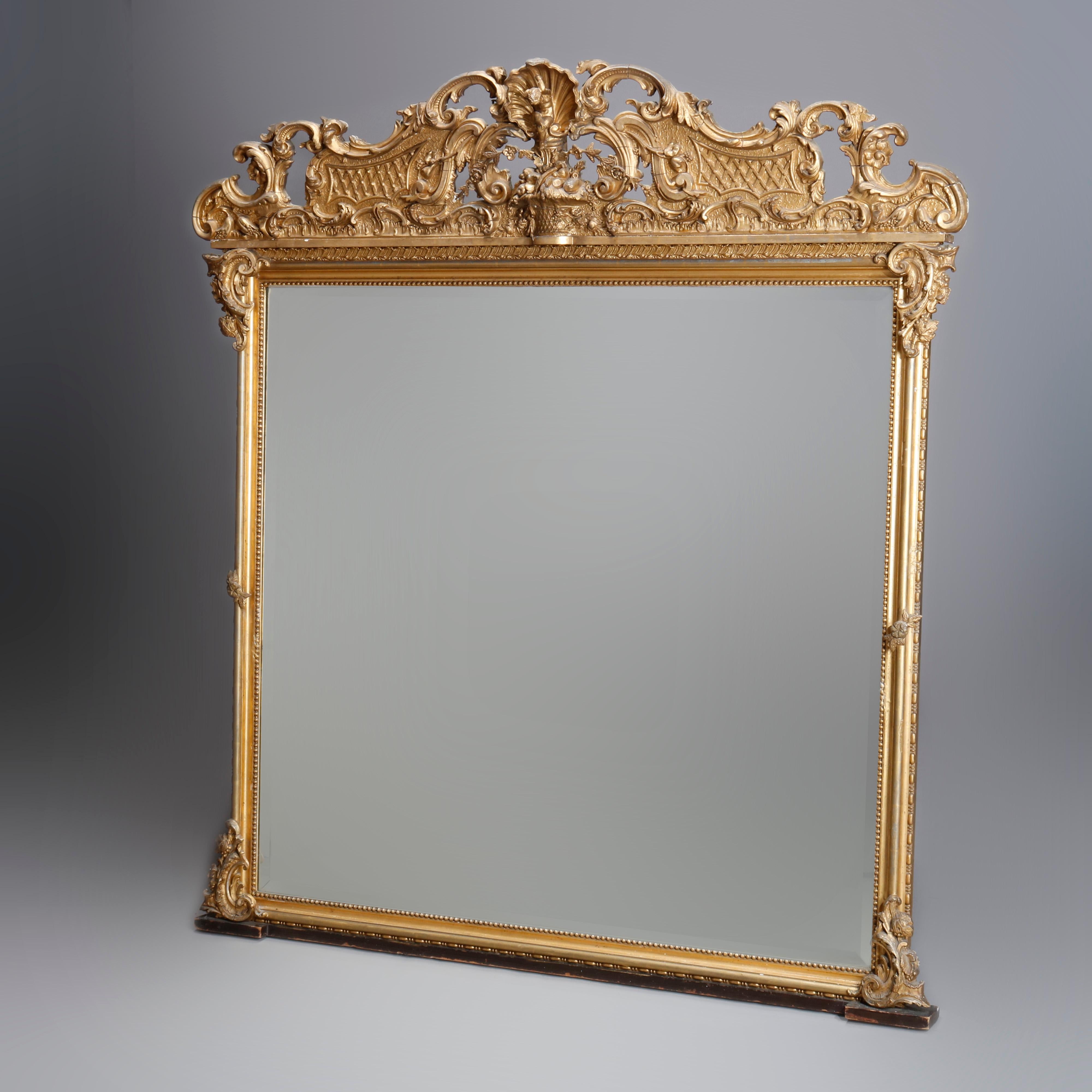 An antique French Louis XIV overmantel mirror offers gold giltwood construction with crest having central panier de fleurs, foliate and scroll elements, frame with beaded trim and scrolled foliate supports, housing beveled mirror, circa