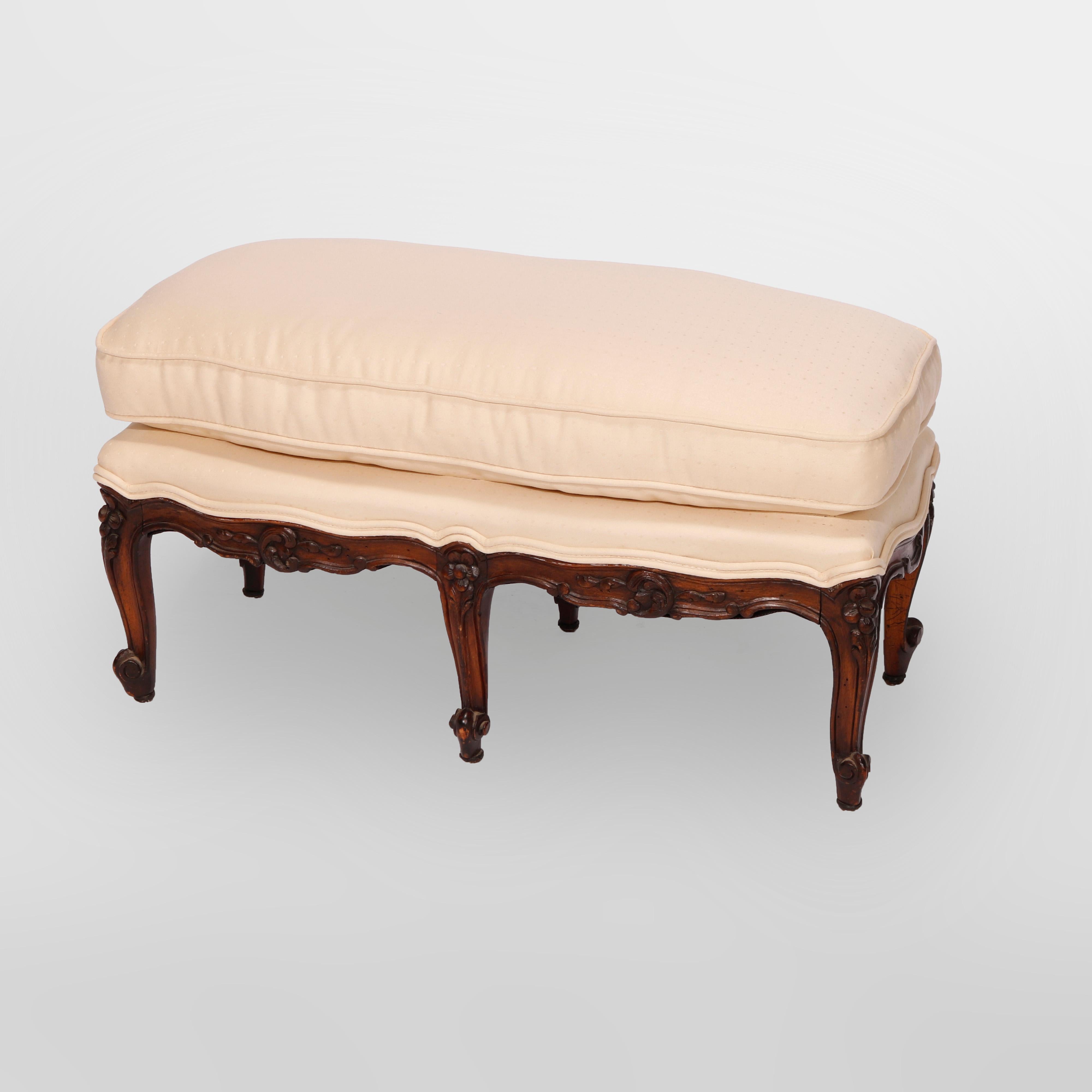 An antique French Louis XIV style ottoman offers upholstered attached cushion over walnut frame with shaped skirt raised on six cabriole legs having carved floral capitals and terminating in stylized scroll feet, 19th century

Measures - 13.75'' H x