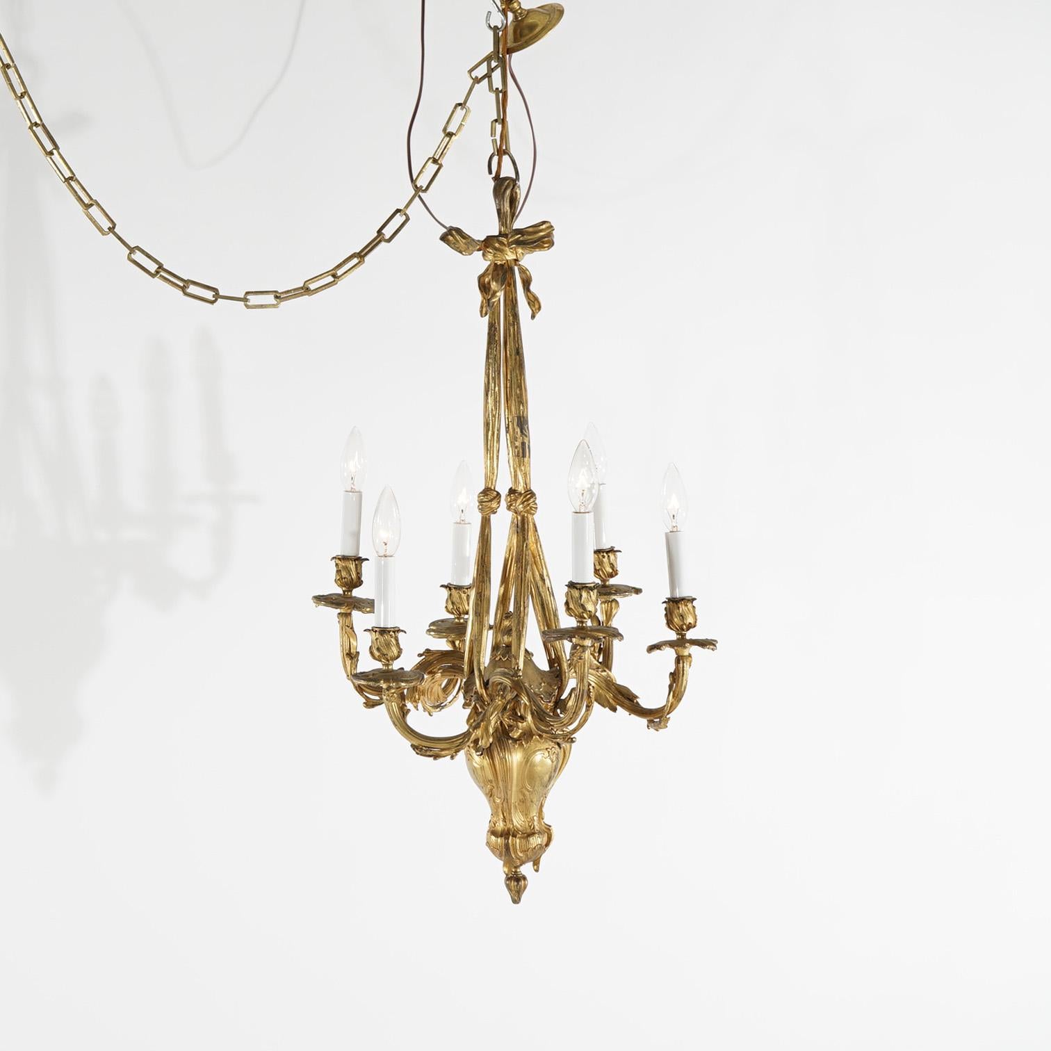 A French Louis XIV style chandelier offers gilt cast bronze frame with stylized urn font having six foliate form scroll arms terminating in candle lights, suspended by drape form drops, c1920

Measures- 32.5''H x 17''W x 17''D; 60'' drop