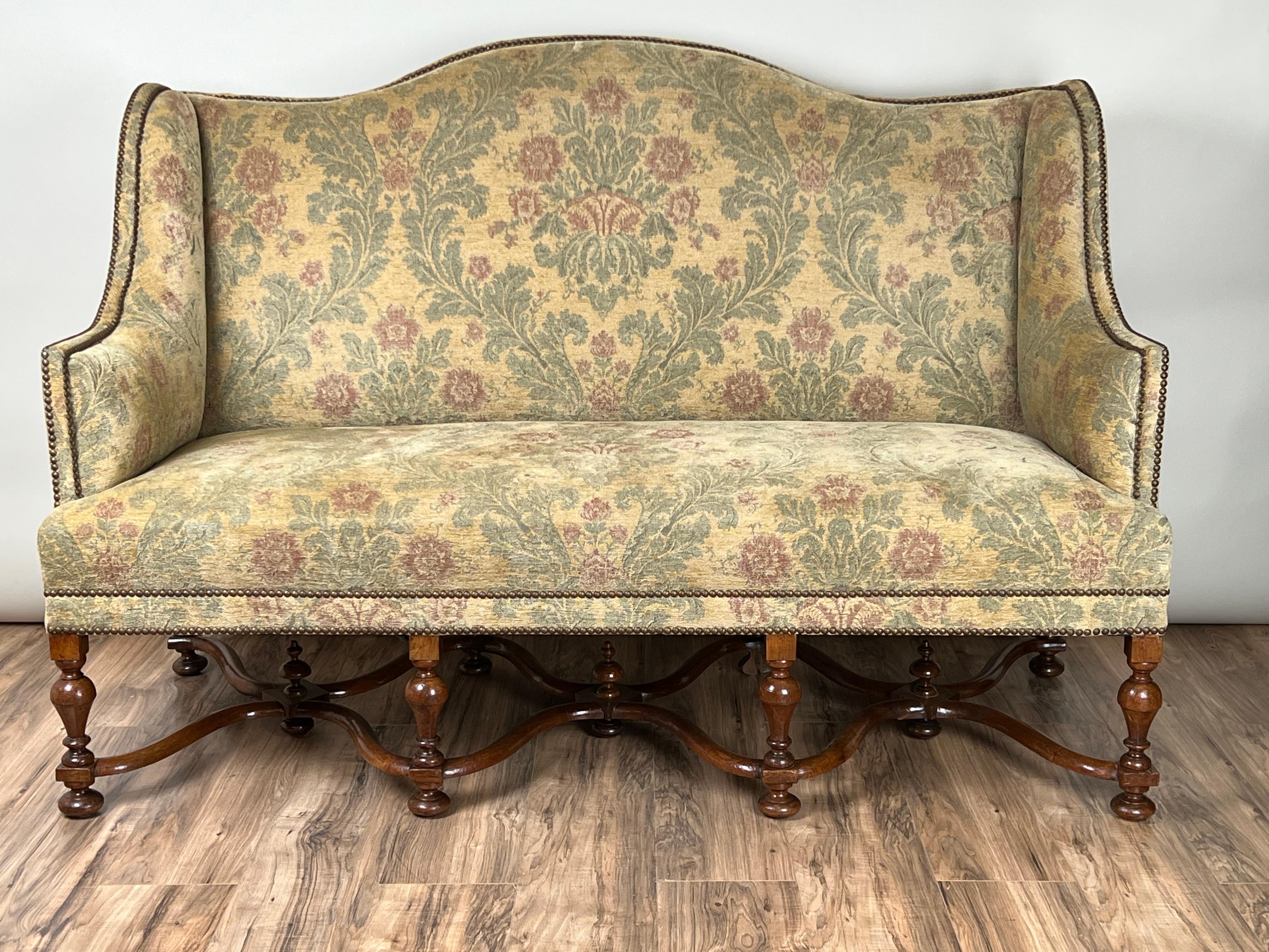 This Antique French Louis XIV Style Highback Settee, dating back to the late 19th century, is a stunning example of neoclassical design. The settee’s high, curved back provides a stately and supportive seating area, while the sumptuous floral fabric