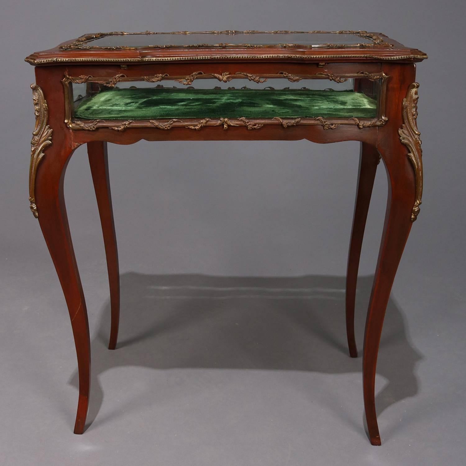 Antique French Louis XIV style lift top velvet lined vitrine curio cabinet table features shaped mahogany display case having beveled glass top with foliate cast bronze framed viewing windows and seated on cabriole legs with cast acanthus mounts,