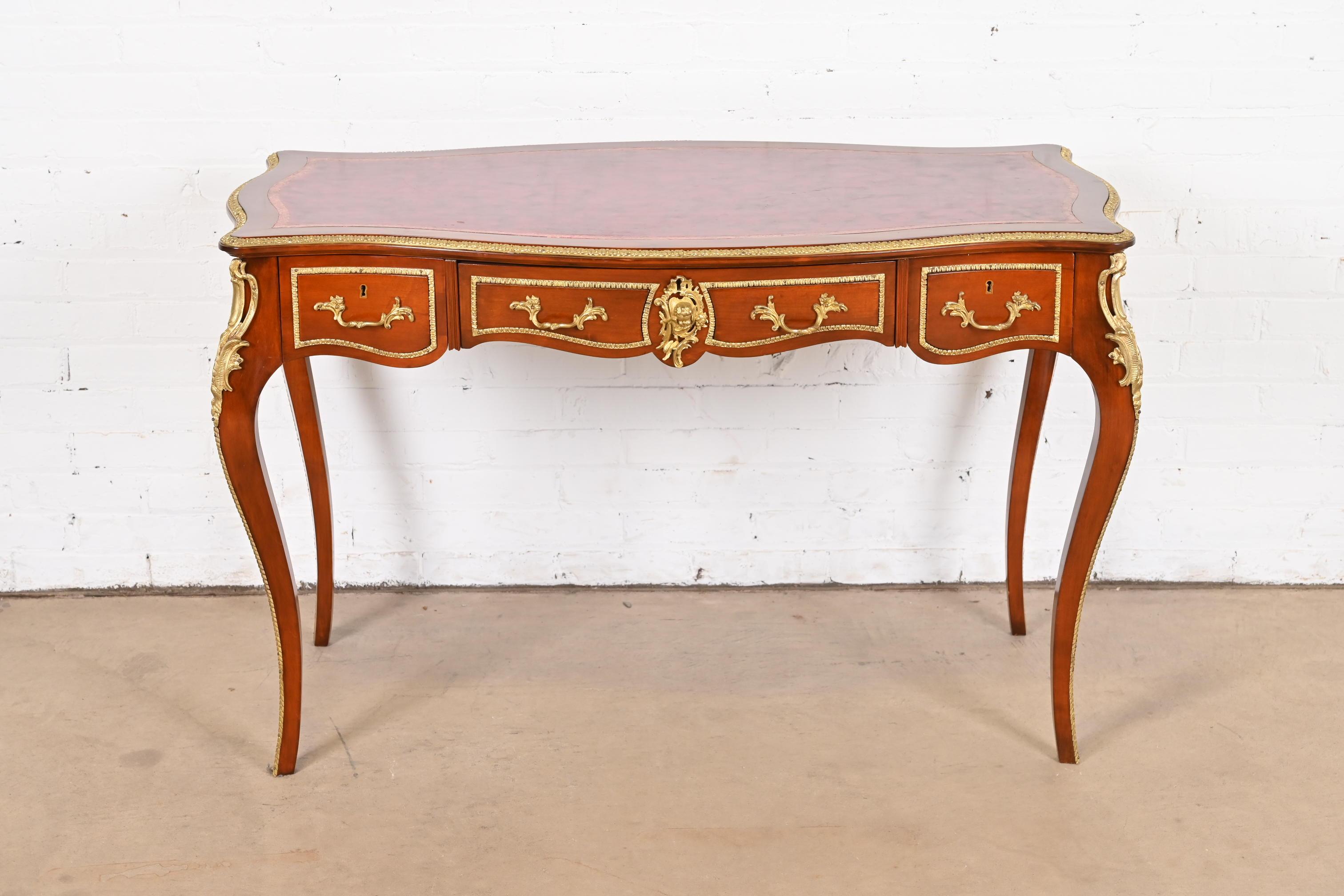 A gorgeous French Louis XV or French Continental style writing desk or bureau plat desk

France, Circa 1940s

Beautiful cherry wood, with red painted faux leather top, and mounted gilt bronze ormolu and hardware.

Measures: 46.5