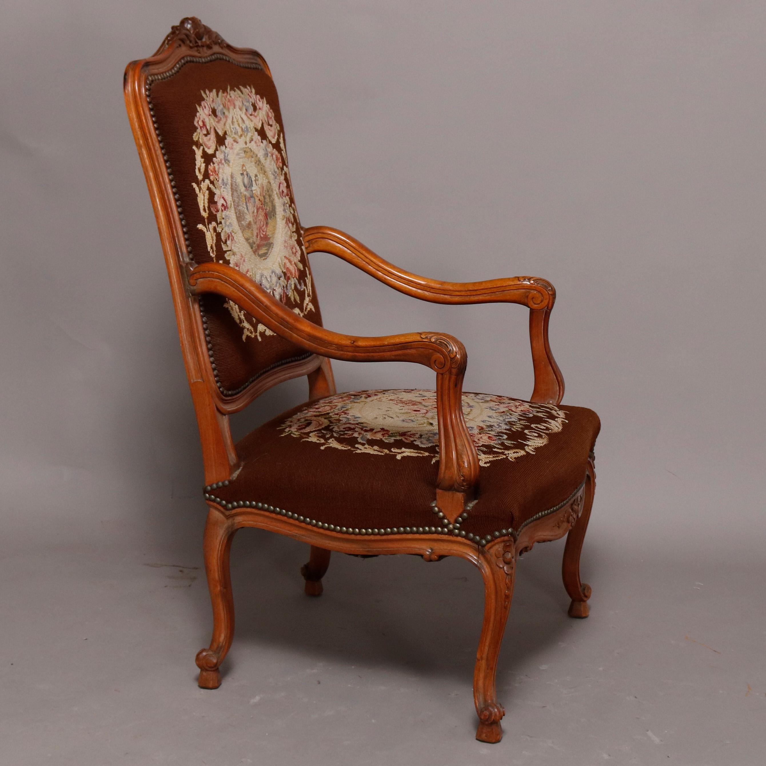 An antique French Louis XV fauteuil offers fruitwood frame with carved floral and foliate crest and skirt, shaped arms and raised on cabriole legs terminating in scroll feet, upholstered in needlepoint with seat having floral reserve and back with