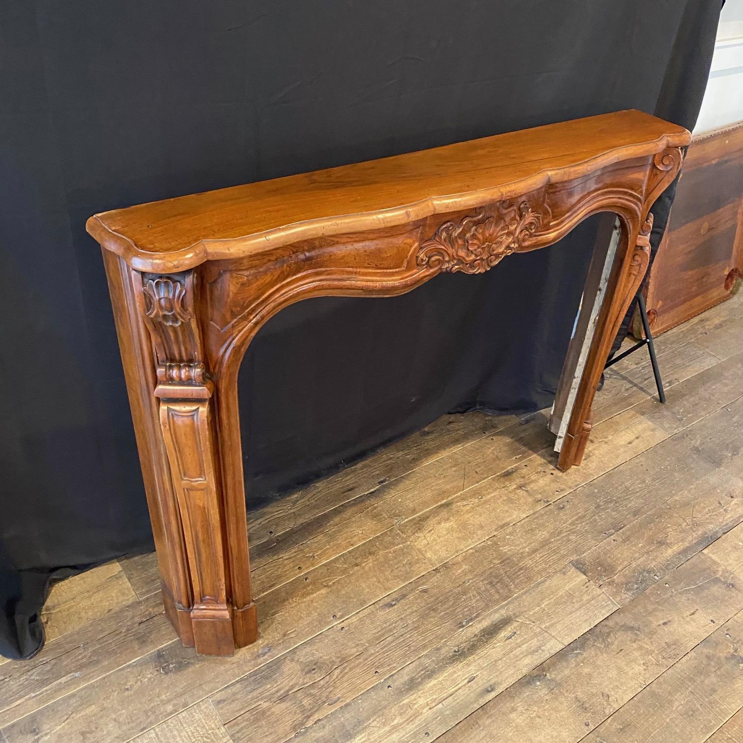 A rare decorative walnut wood hand carved Louis XV style 19th century French fireplace mantel -- finely carved detailed shell, foliage, scrolled swags, supported on solid carved plinths. The spandrels with conforming, flowing swags, All beneath a