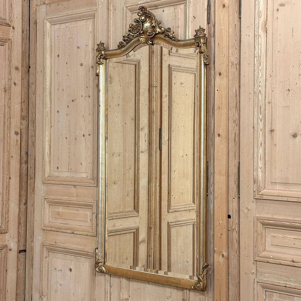 Le miroir ancien en bois doré Louis XV ajoute l'élégance des mouvements rococo et baroque à n'importe quel décor !  La couronne arquée est ornée de coquillages stylisés, de motifs floraux et de feuillages. Les ornements tombent en cascade sur