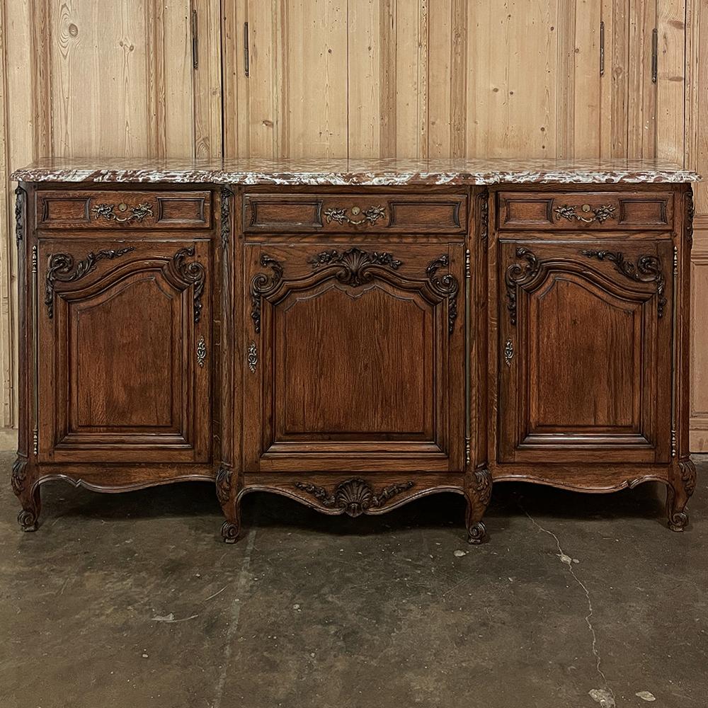Antique French Louis XV step-front marble top serpentine buffet is an exceedingly elegant expression of the style, with motifs carried over from the prior Louis XIV style expressed in more delicate realizations. The subtle scroll of the serpentine
