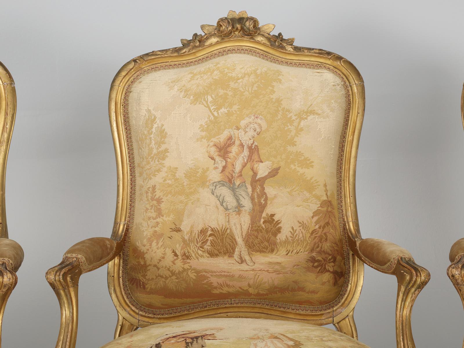 Antique French Louis XV style arm chairs in a suite of (4) matching antique French arm chairs in their original Aubusson inspired thick fabric. The gilded frames are original and have been structurally restored, but cosmetically left original. The