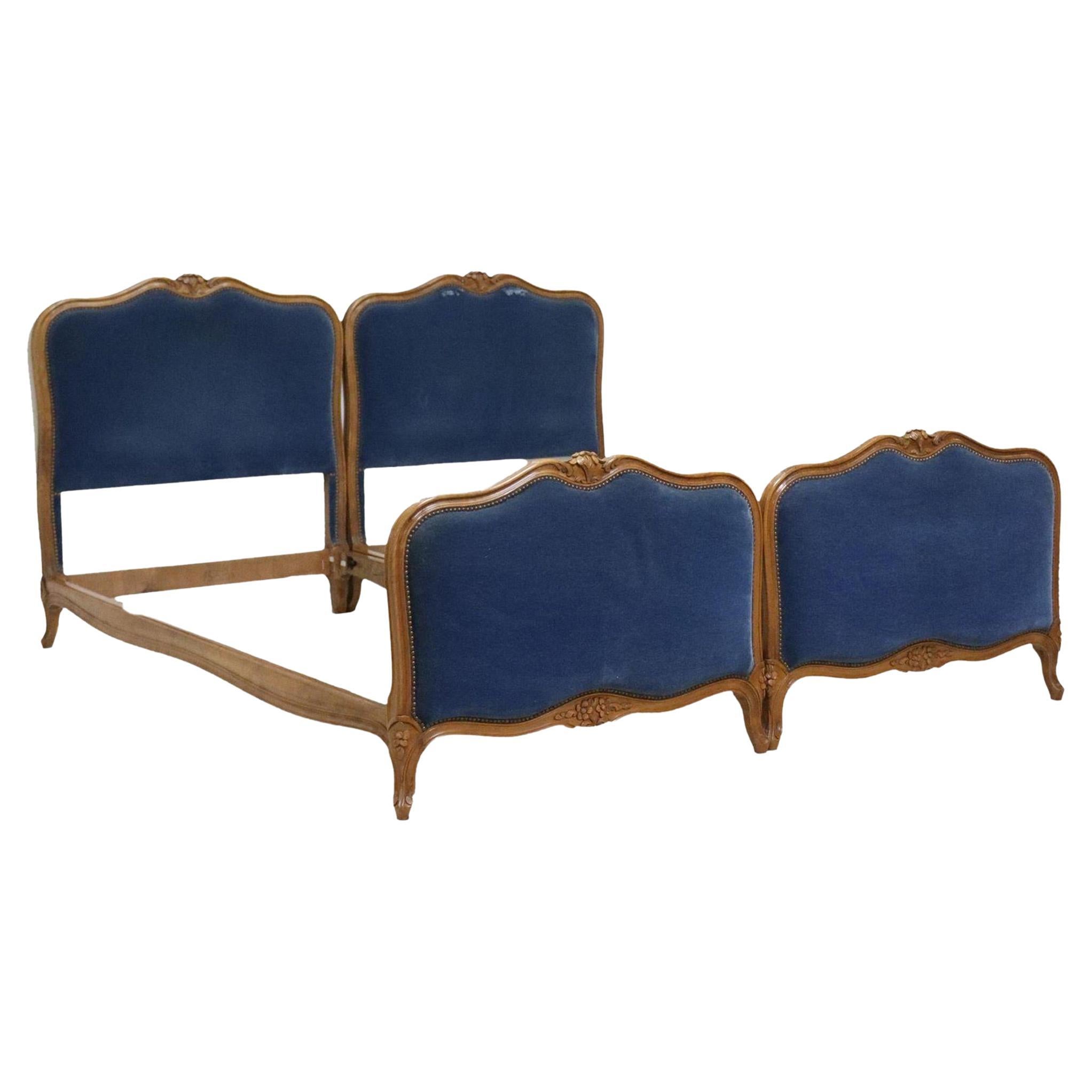 A lovely pair of antique French Louis XV style beds, 20th c. Each bed frame features carved floral crest, shaped frame in padded blue velvet upholstery, with nailhead trim, rising on cabriole legs, ending on whorl feet.

Dimensions
exterior: approx
