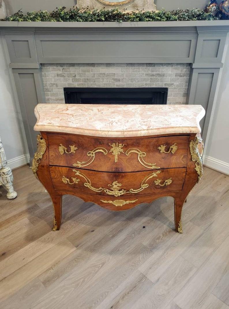 A stunning French Louis XV bombe marble-top chest of drawers commode from the 19th century, styled in the manner of Charles Cressent (France, 1685–1768), finished in luxurious Rocco taste, featuring exotic well figured burled wood, hand-crafted in a