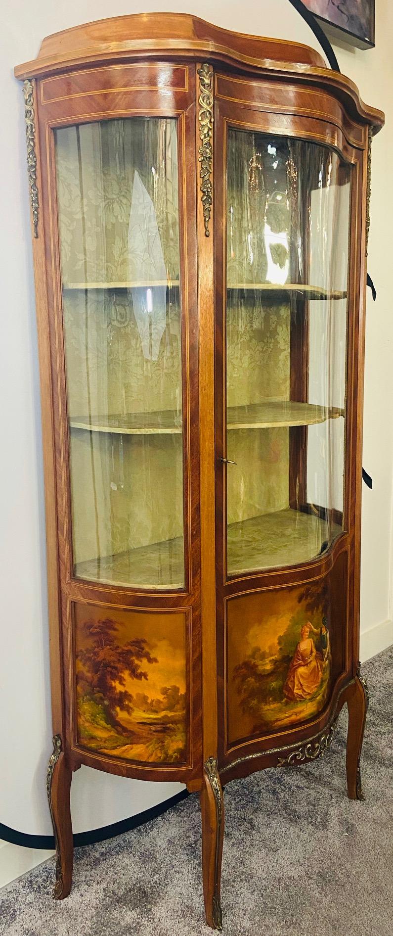 A quality antique French Louis XV style display cabinet or vitrine featuring acanthus and floral bronze mounted design and hand painted wood panels showing stunning landscape scenes as well as a portrait of a man and woman in the middle. With three