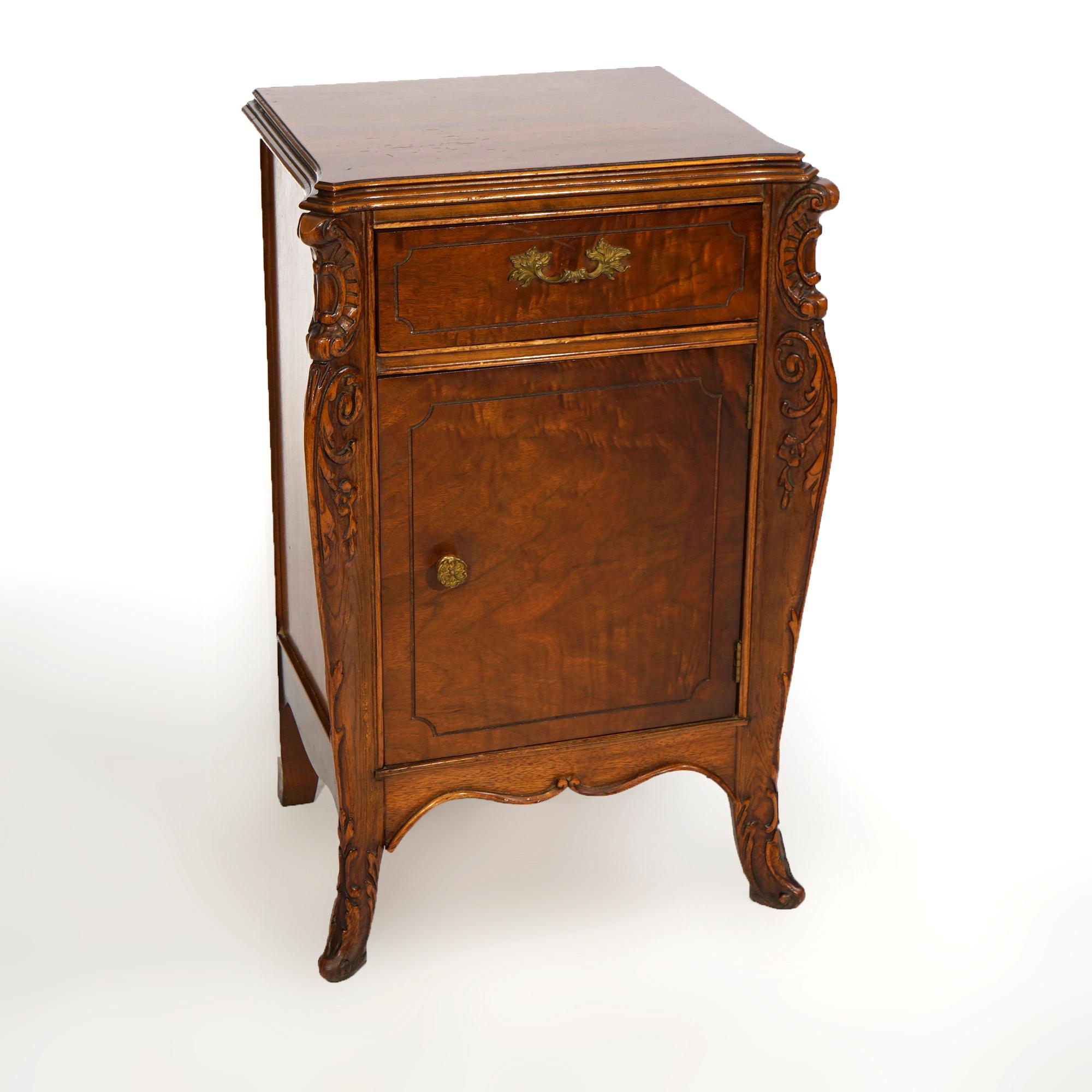 An antique French Louis XV style French side cabinet offers mahogany construction with shaped and beveled top over case with upper drawer over single door cabinet with flanking scroll and foliate elements, raised on feet with carved acanthus feet,