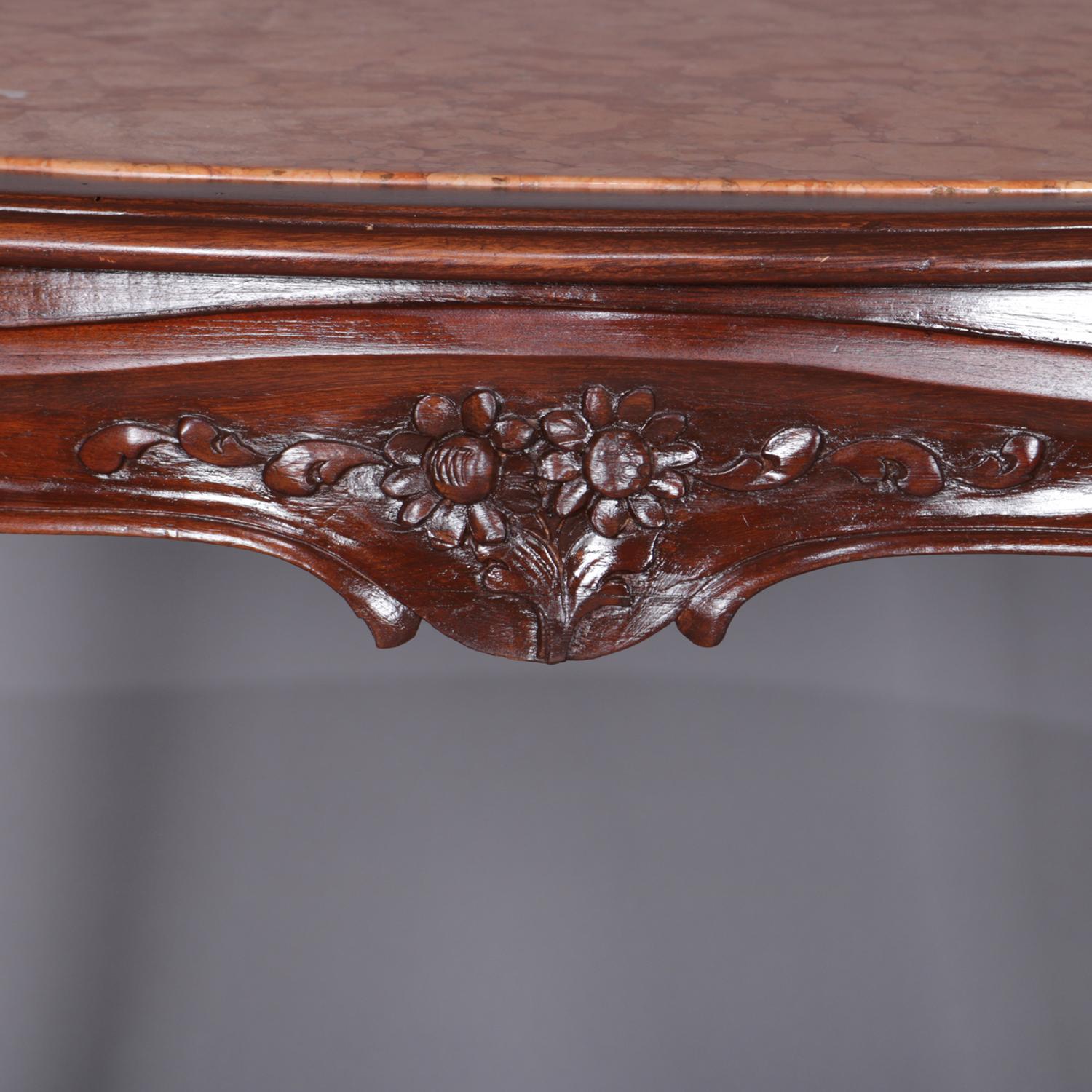An antique French Louis XV style center table features inset marble top surmounting walnut frame with scalloped apron having carved foliate and floral decoration, raised on cabriole legs joined by cross stretcher having scroll form arms and central