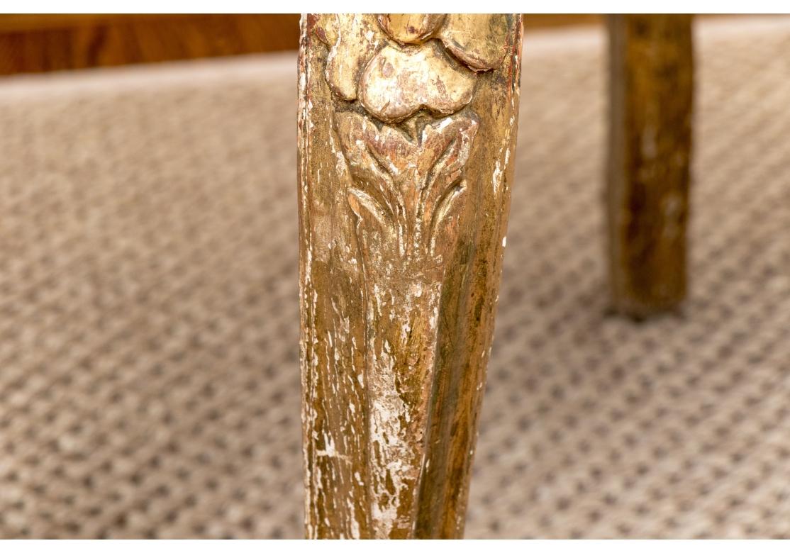 Ca. XVIIIe siècle. Ample banc de toilette français ancien, sculpté et doré, avec un dossier ajouré et nervuré, et un groupe de roses sculptées sur la crête. La large barre d'assise est ornée d'un motif central sculpté et repose sur des pieds avant