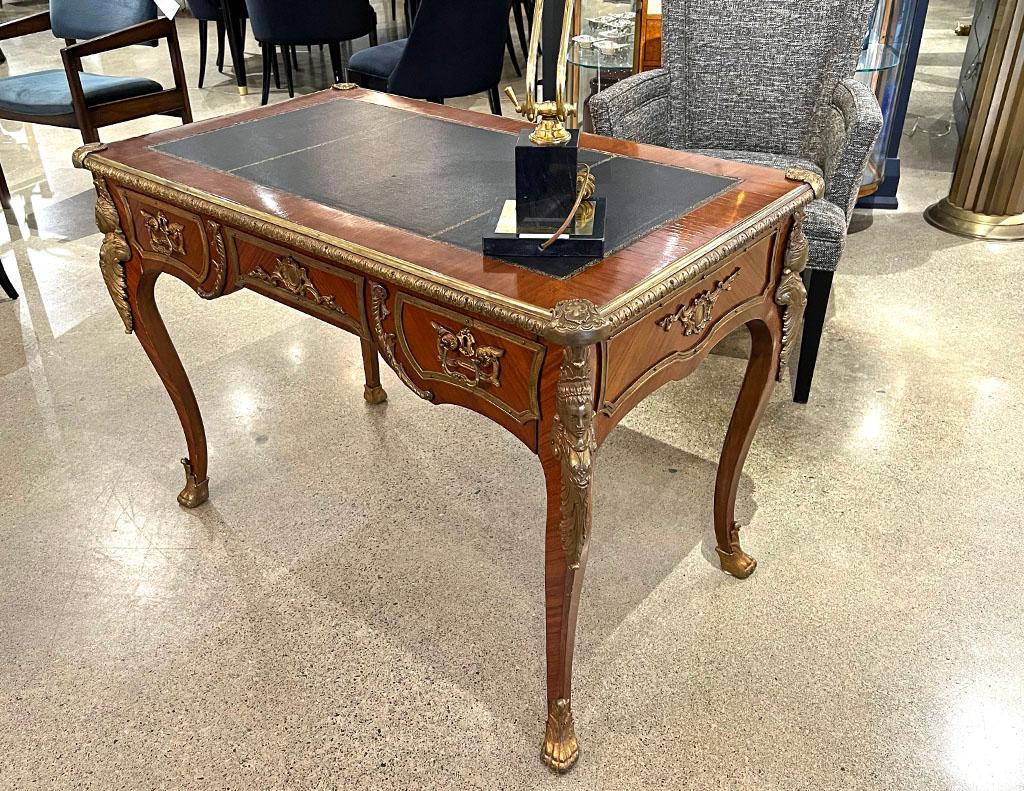 Antique French Louis XV style gilt bronze mounted leather top writing desk. This elegantly sculpted desk hails from France, late 19th Century. Features magnificently sculpted gilt bronze detailing with gold embossed black leather top. Price includes