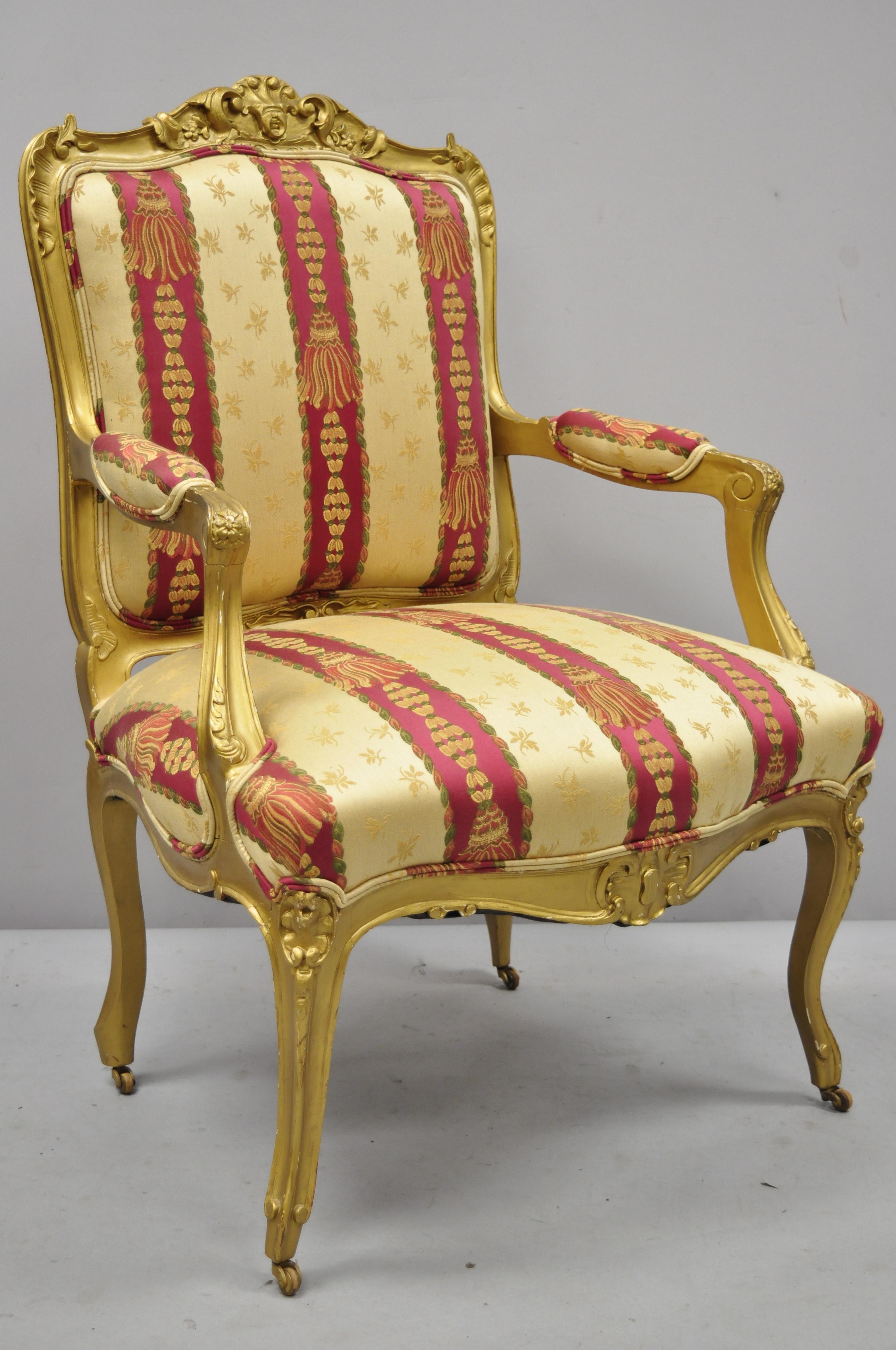 Antique French Louis XV style gold gilt parlor arm lounge chair. Beautiful tassel printed pink and gold fabric, rolling casters, solid wood frame, upholstered armrests, nicely carved details, cabriole legs, very nice antique item, great style and