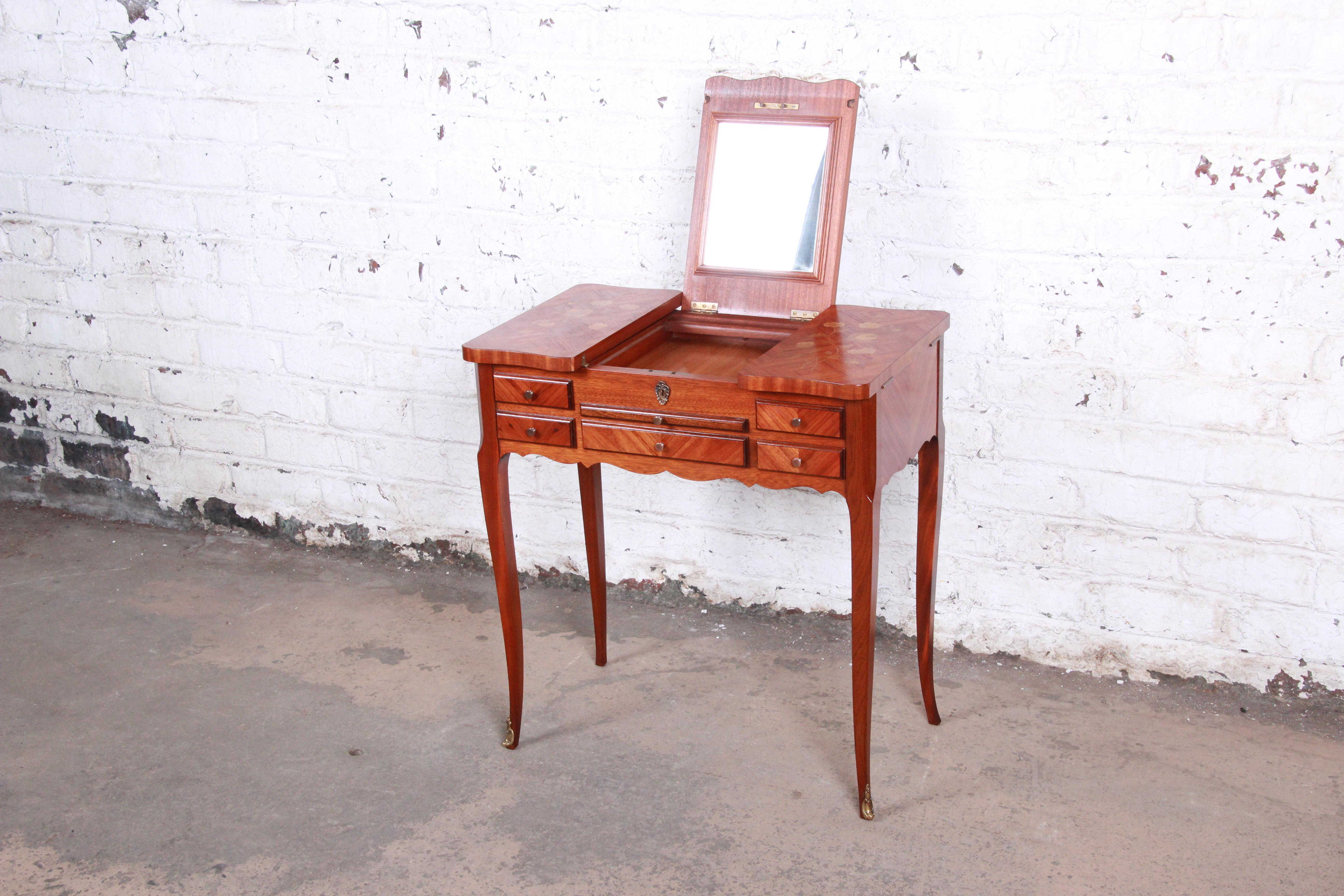 An exceptional antique French Louis XV style vanity, circa 1930s. The vanity features stunning mahogany wood grain with beautiful inlaid floral marquetry and tall cabriole legs. It has a flip-up mirror with storage compartments on each side, a