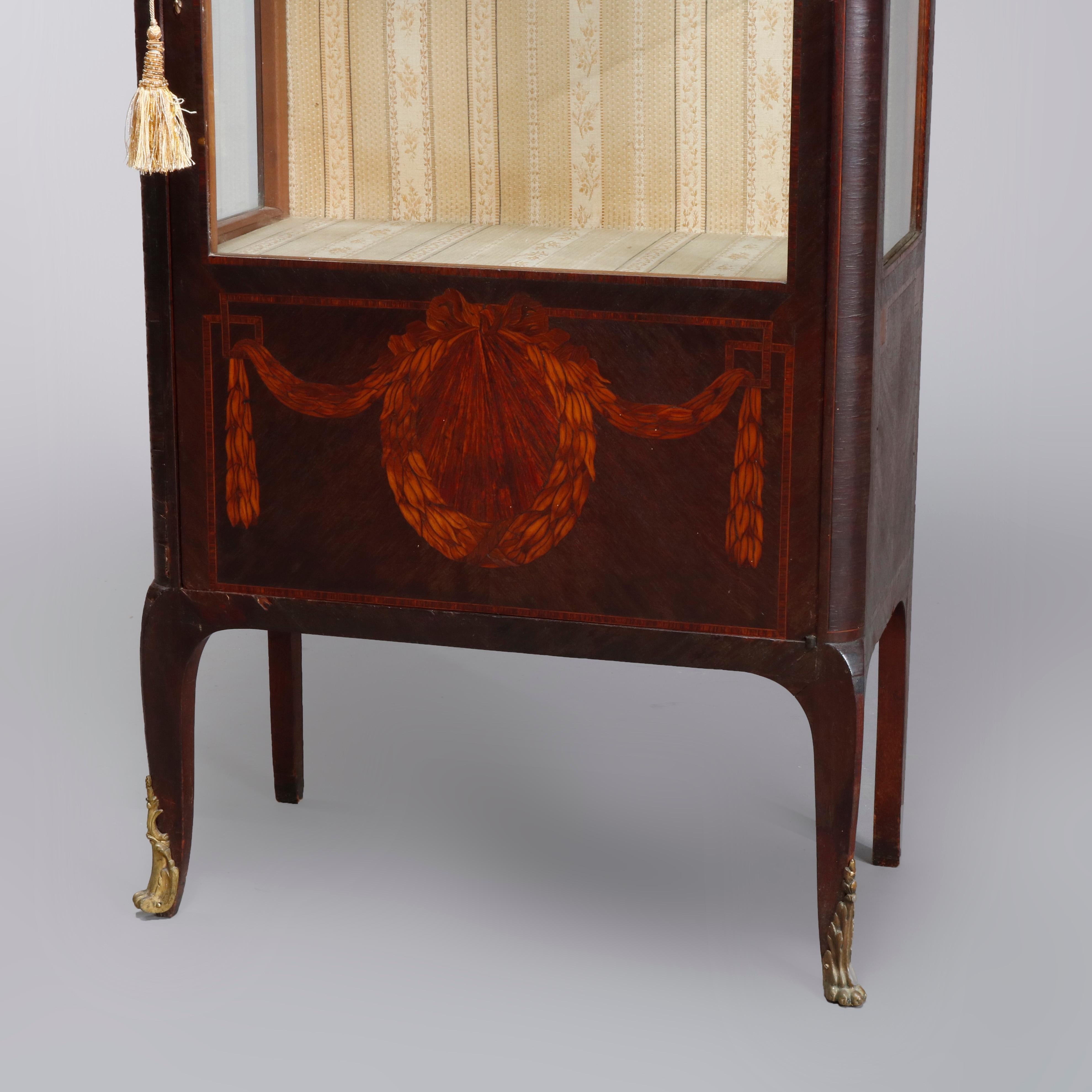 An antique French Louis XV style vitrine offers mahogany case with marble top surmounting mahogany case with scroll, foliate and garland marquetry, single glass door and foliate cast ormolu mounts, with key, circa 1890

Measures: 56.75
