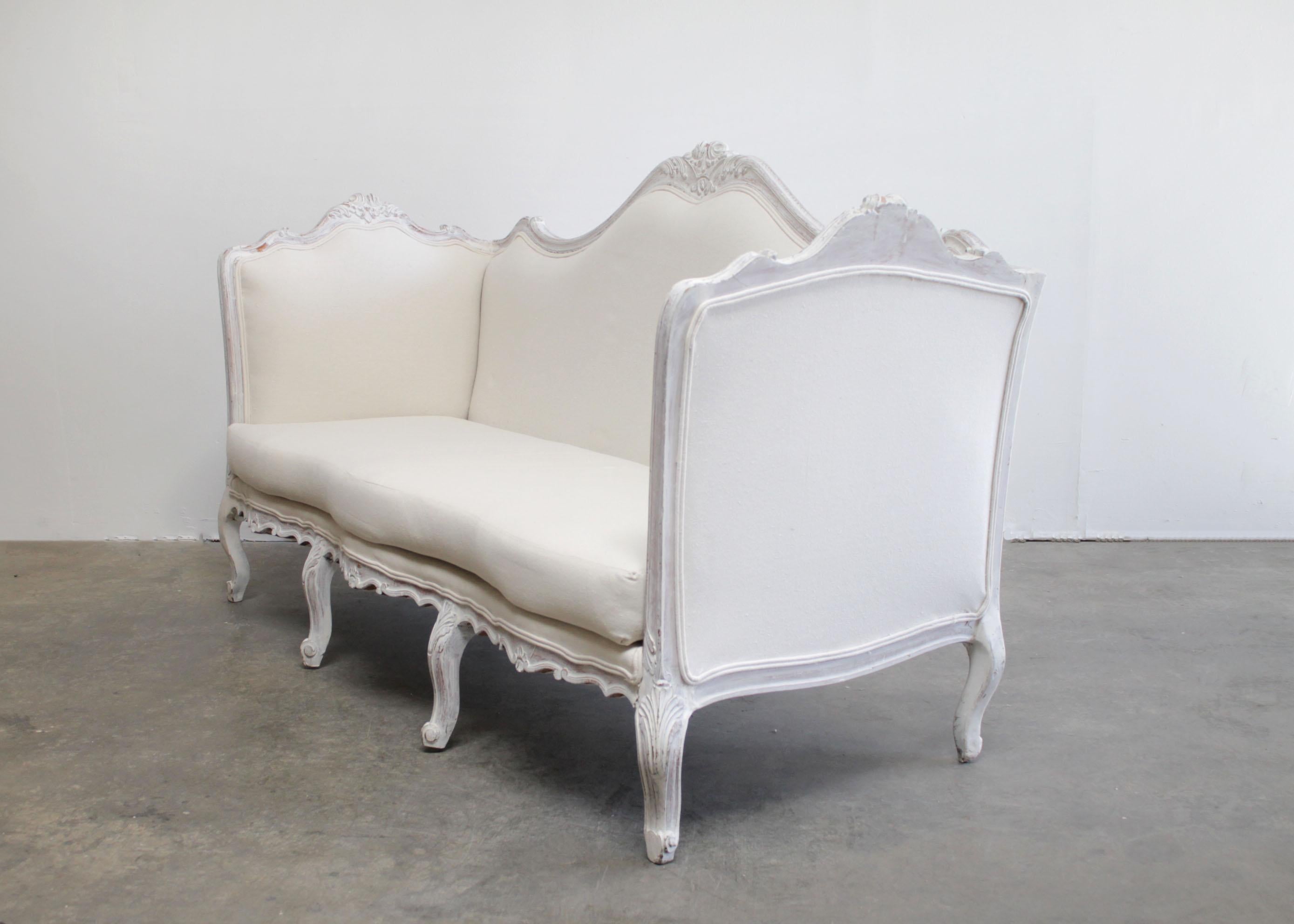 Antique French Louis XV style painted and upholstered sofa.
Beautiful painted sofa in soft white with subtle antique distressing.
An oyster grey hue, with wood flecks peeking through the paint.
Soft rounded scrolls, and hand carved flowers, and