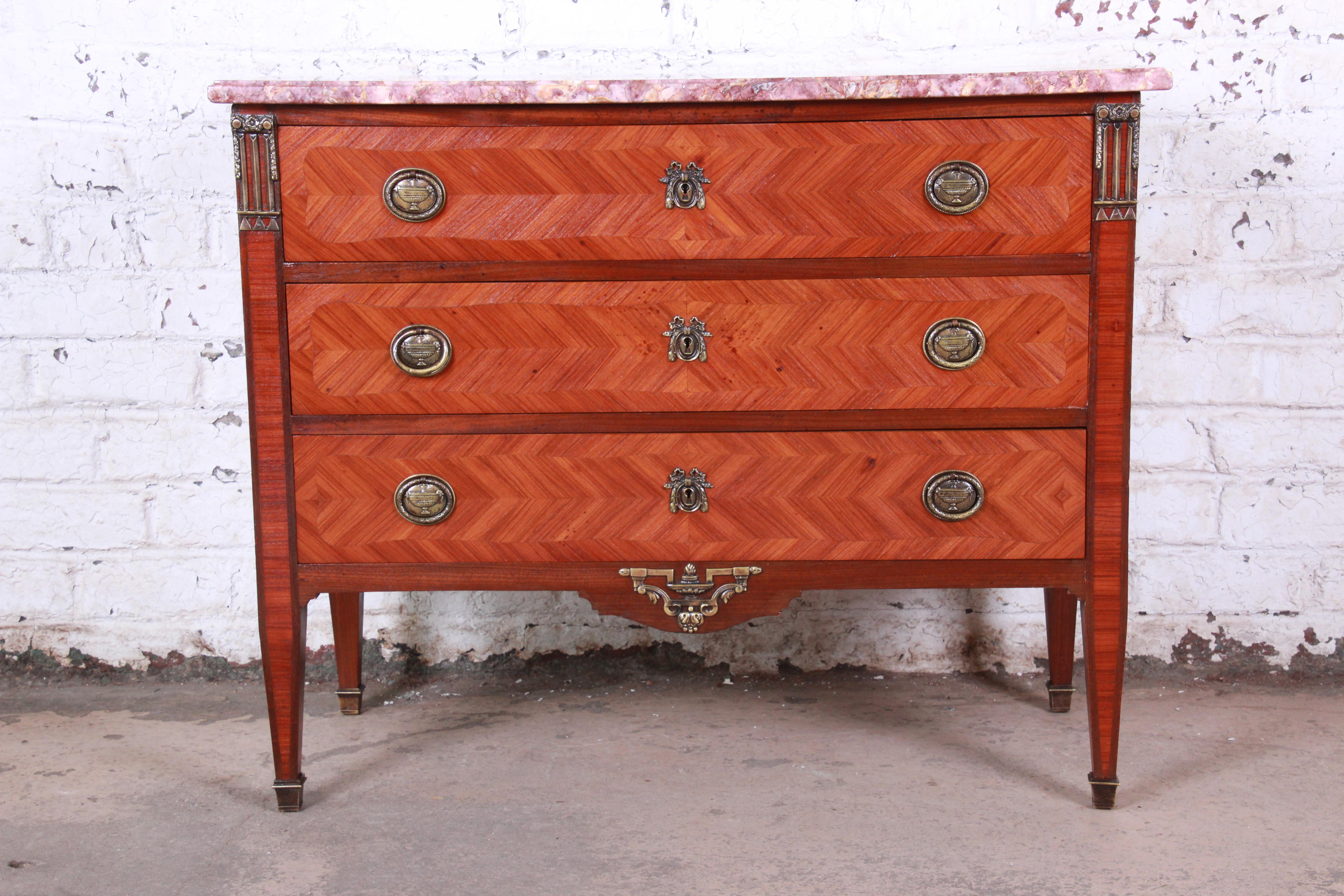 An exceptional antique Louis XV style mahogany chest of drawers or commode. The chest features gorgeous mahogany wood grain, with inlaid parquetry and bronze mounted ormolu. The fuchsia and tan beveled marble top shows incredible veining. The
