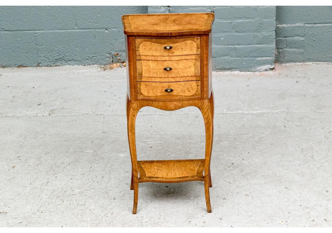A petite and stylish French Drawer Stand. The antique two tone wood French stand has a shaped banded top with a different wood book matched inset panel. The case with three banded drawers with a matching different wood shaped panel over the three.