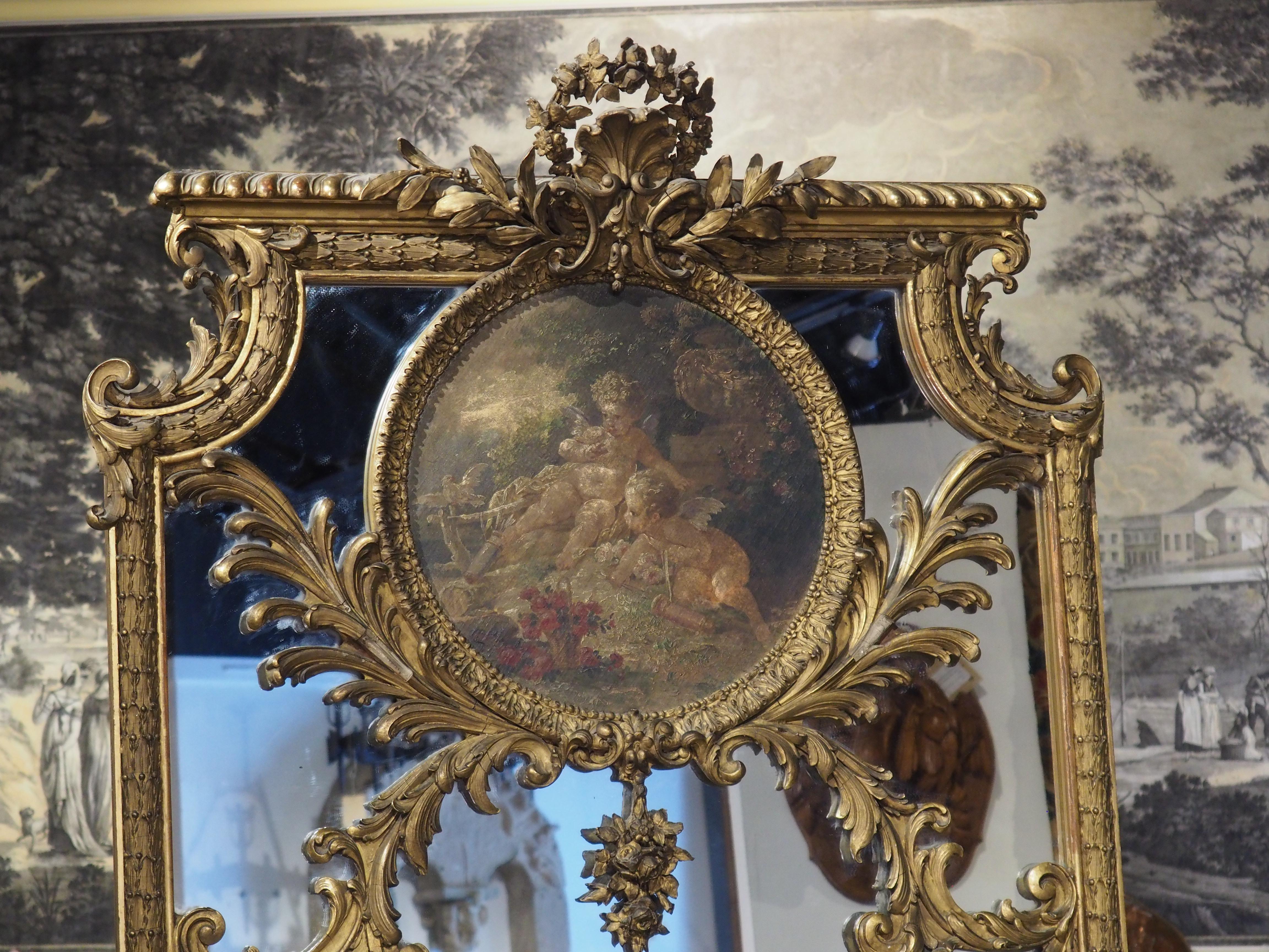 Produced in France, in the late 1800’s, this Louis XV style trumeau mirror features an oil on canvas painting. The 15 ½ inch diameter circular painting depicts two cupids sitting on the ground, watching a dove land on a perch. A basket of red roses