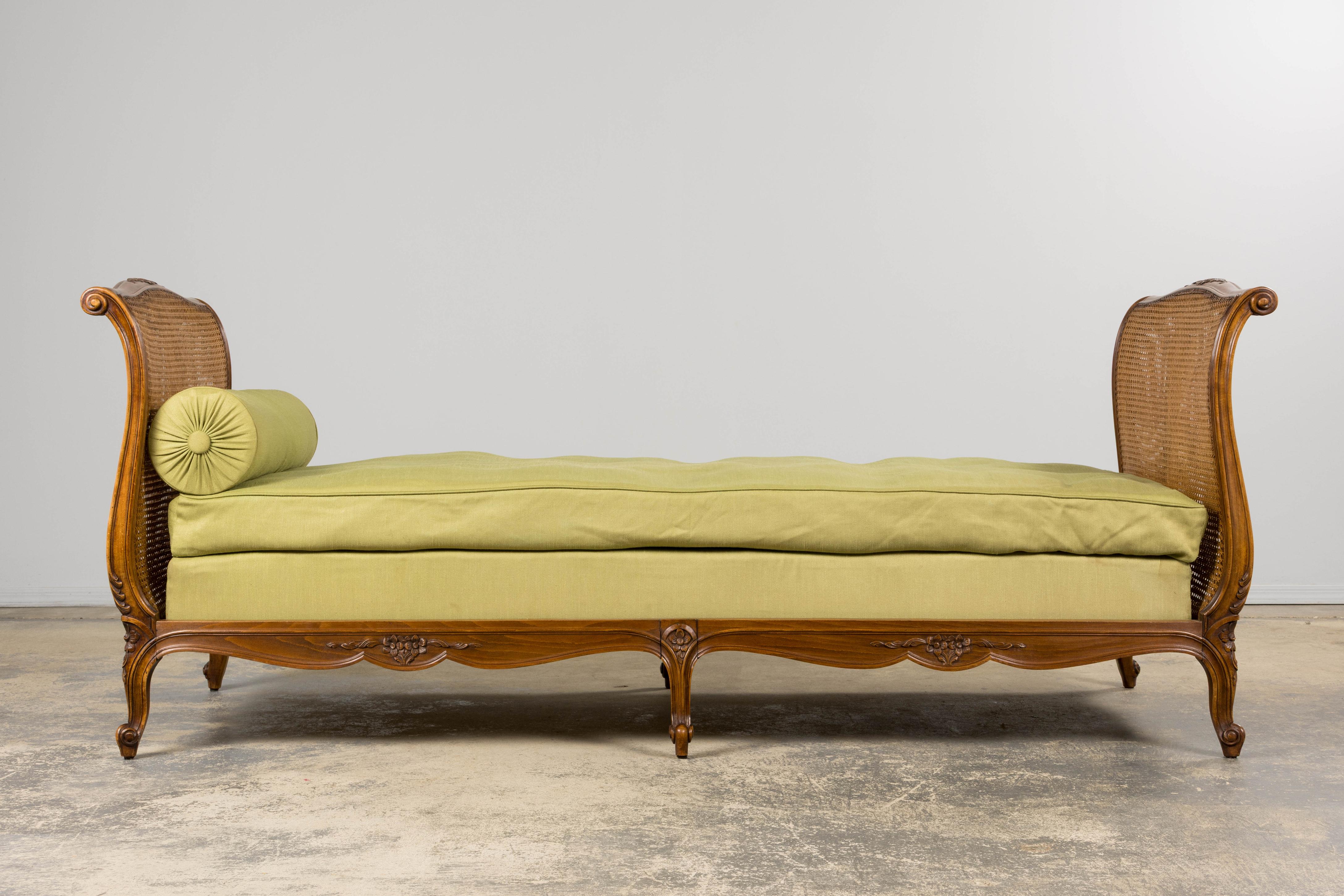 An exquisite late 19th century French provincial daybed in the Louis XV style, sourced from Provence, France. Hand-crafted from solid walnut with sleigh-form ends, each framed in its original hand-woven cane. The carved frame rests on short cabriole