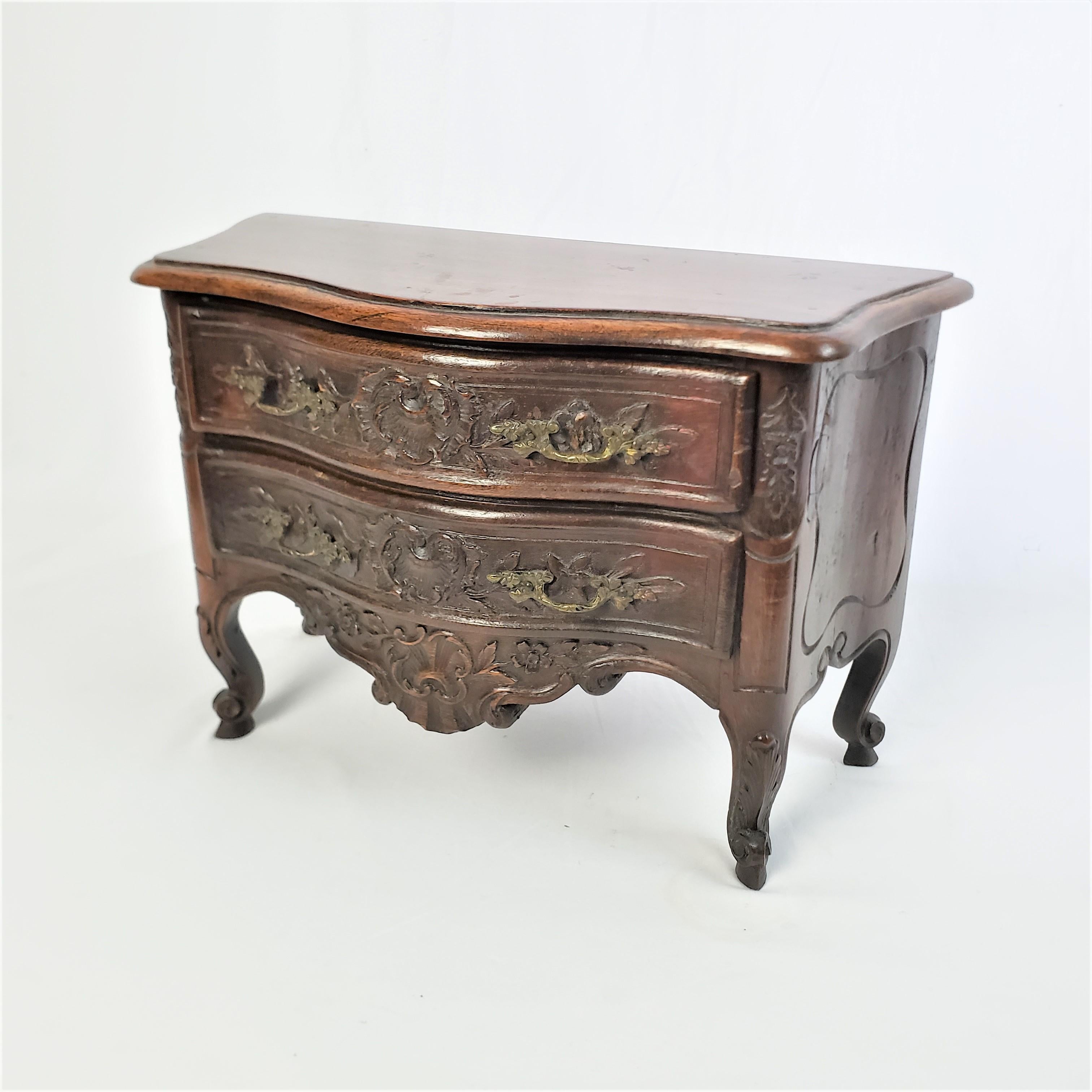 This miniature antique two drrawer dresser is unsigned, but presumed to have originated from France and date to approximately 1850 and done in the period Louis XV style. The dresser is composed of walnut with a serpentine shaped from with carved