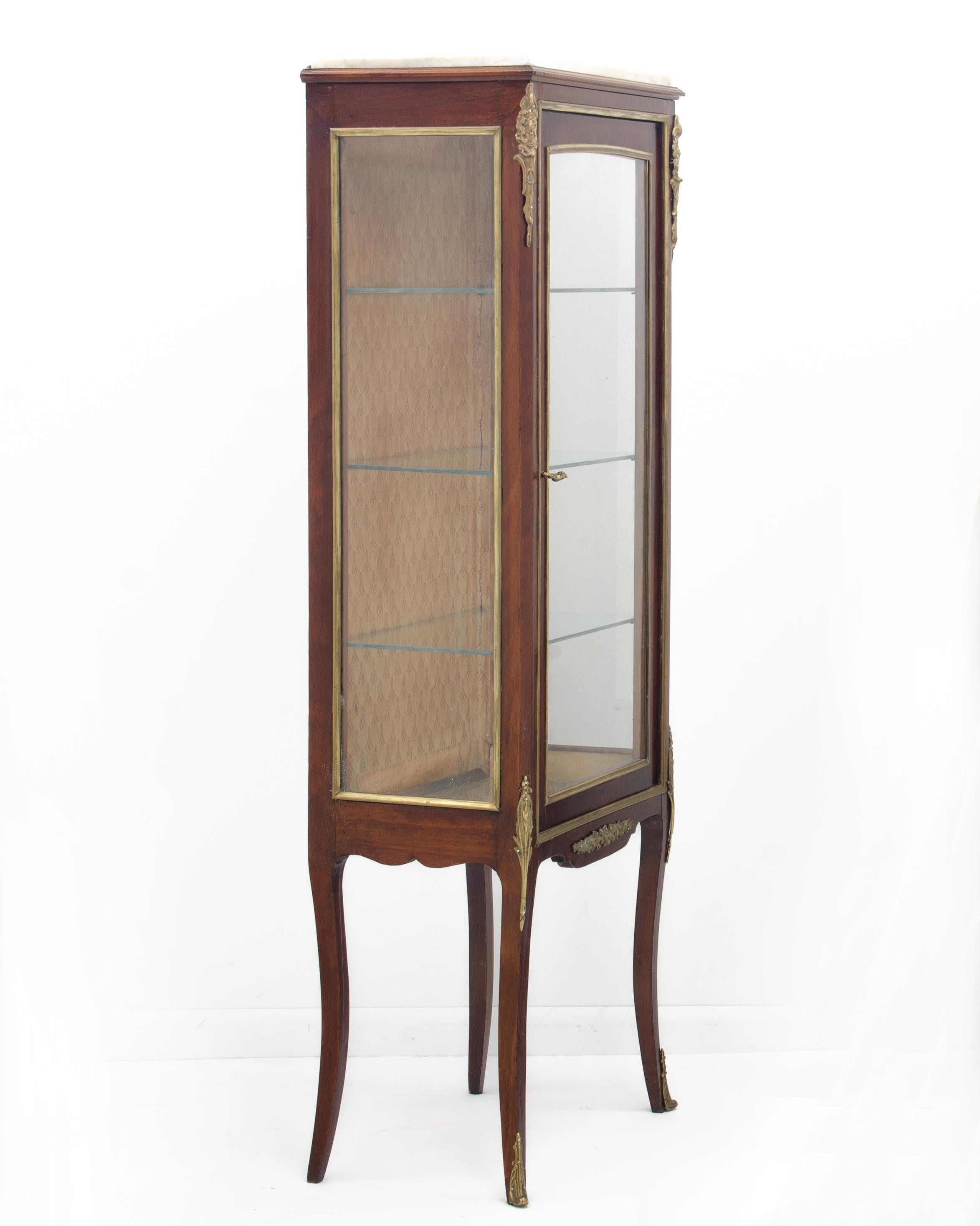A petite French display cabinet or vitrine from the early 20th century. Fruitwood & ofoliate cast ormolu mounts throughout, fabric backing & white marble top. 
Complete with lock and key.